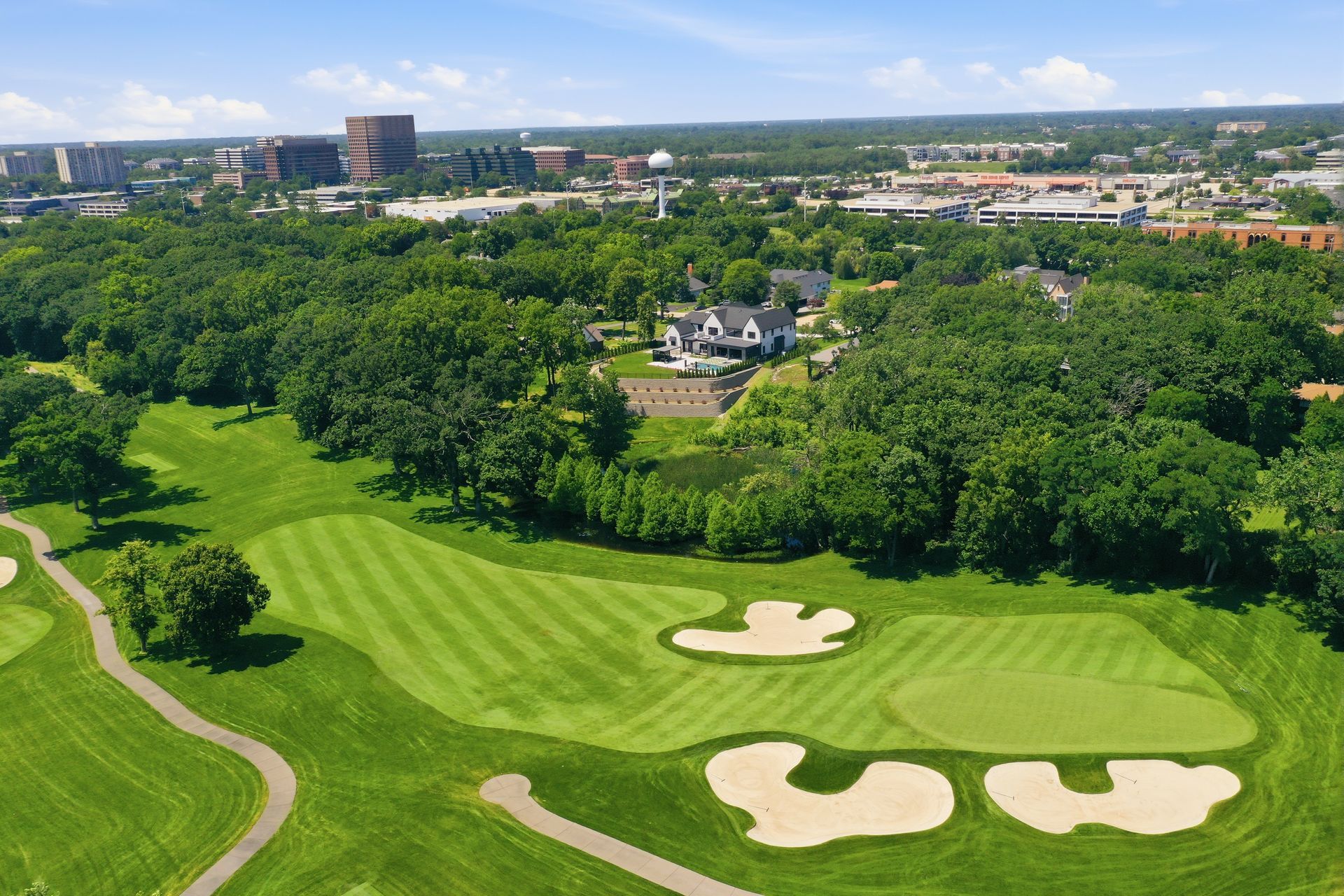 Aerial view of a lush golf course with fairways, sand bunkers, and surrounding trees under a clear sky