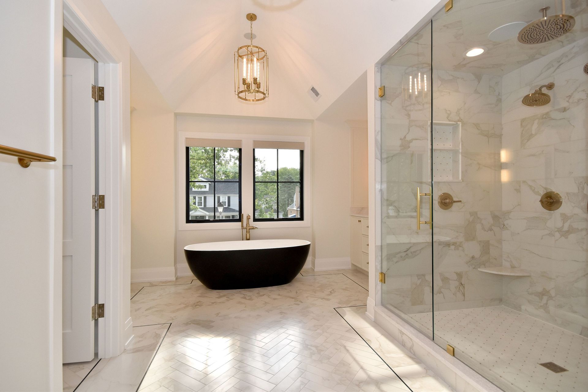 Bright modern bathroom with freestanding tub, glass shower, and window view