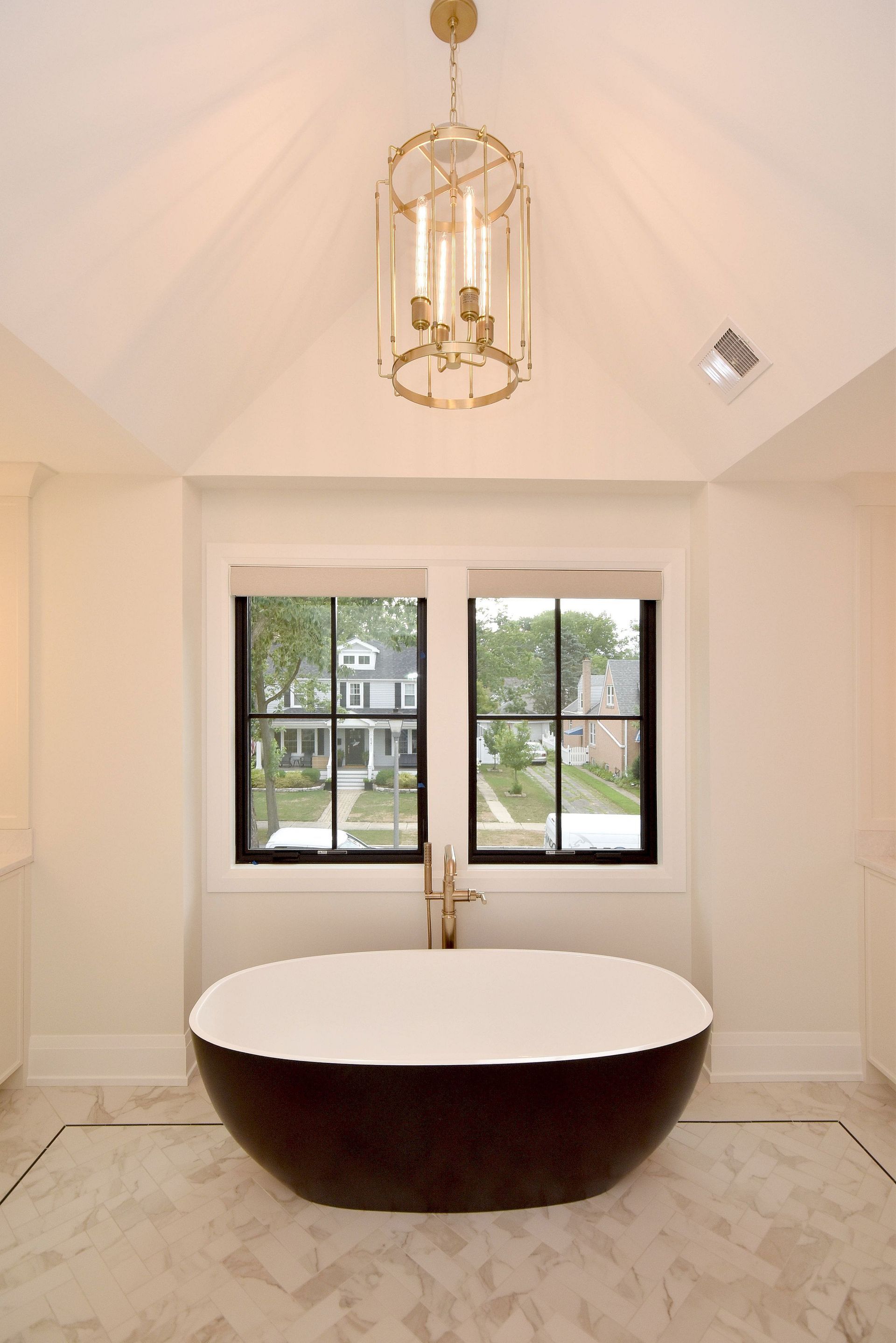 Modern bathroom with a freestanding oval tub, gold chandelier, and window view outside