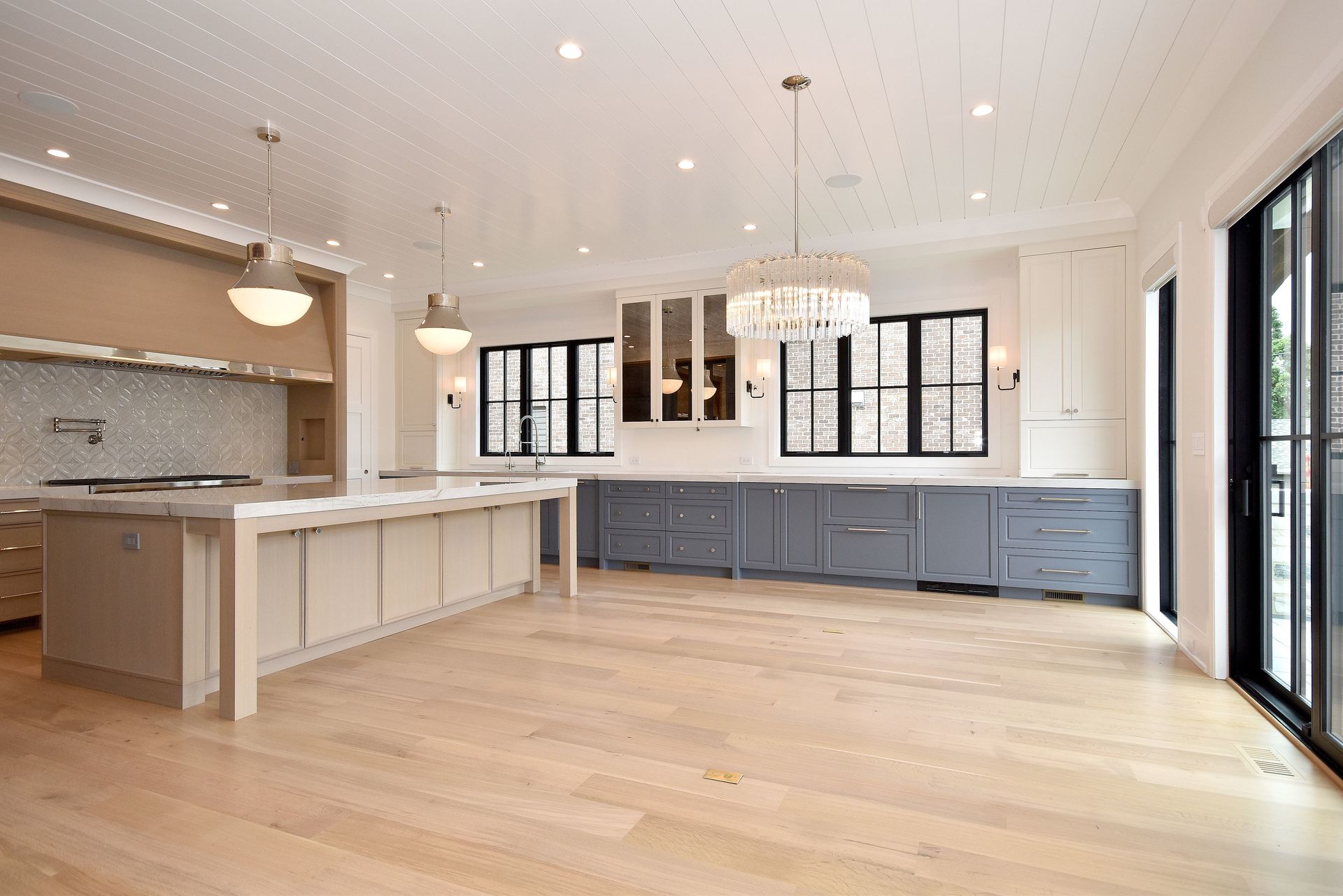 Bright modern kitchen with white cabinets, blue island, wood floors, and large windows