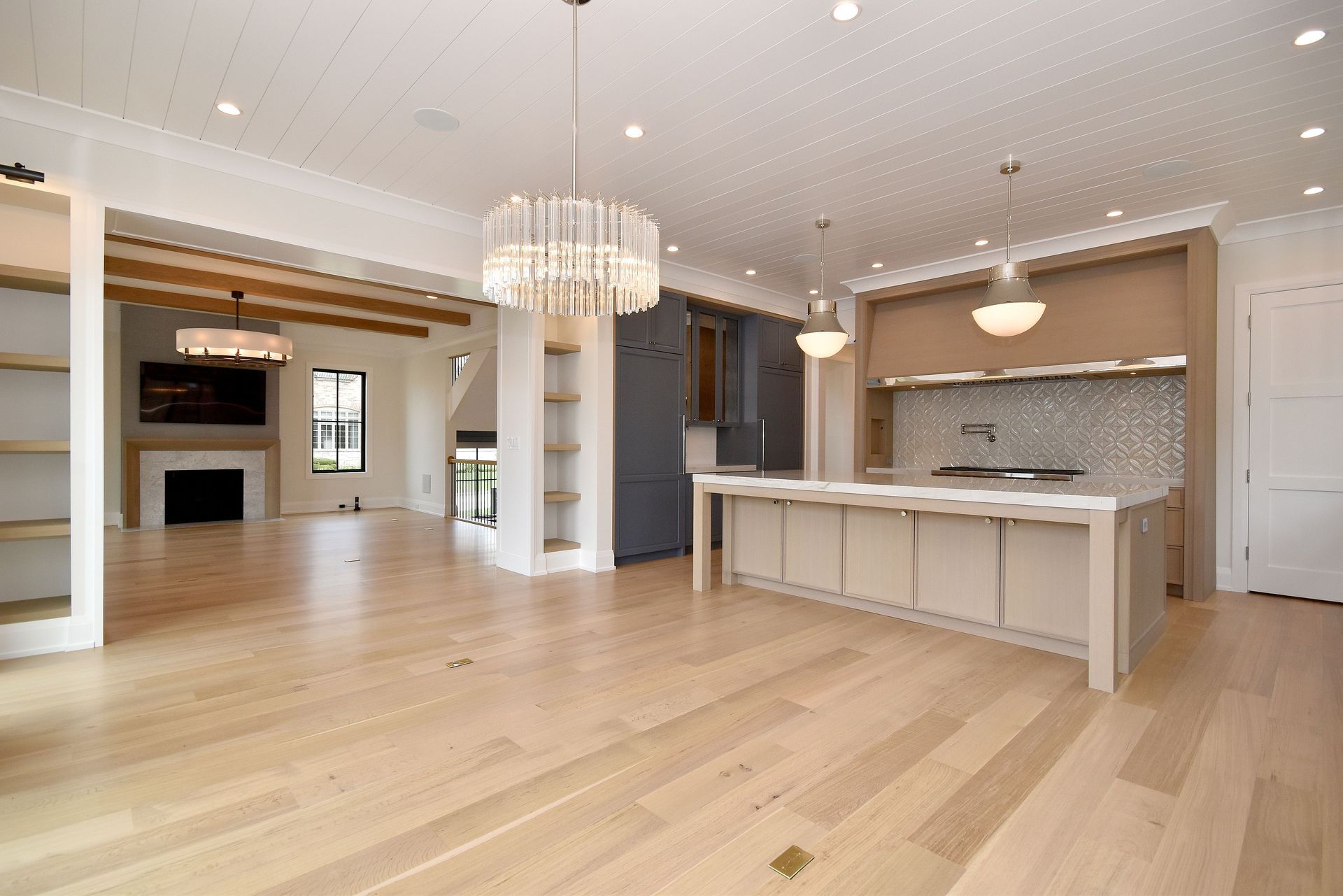 Spacious modern open-plan kitchen and living room with light wood floors, white cabinets, and chandeliers