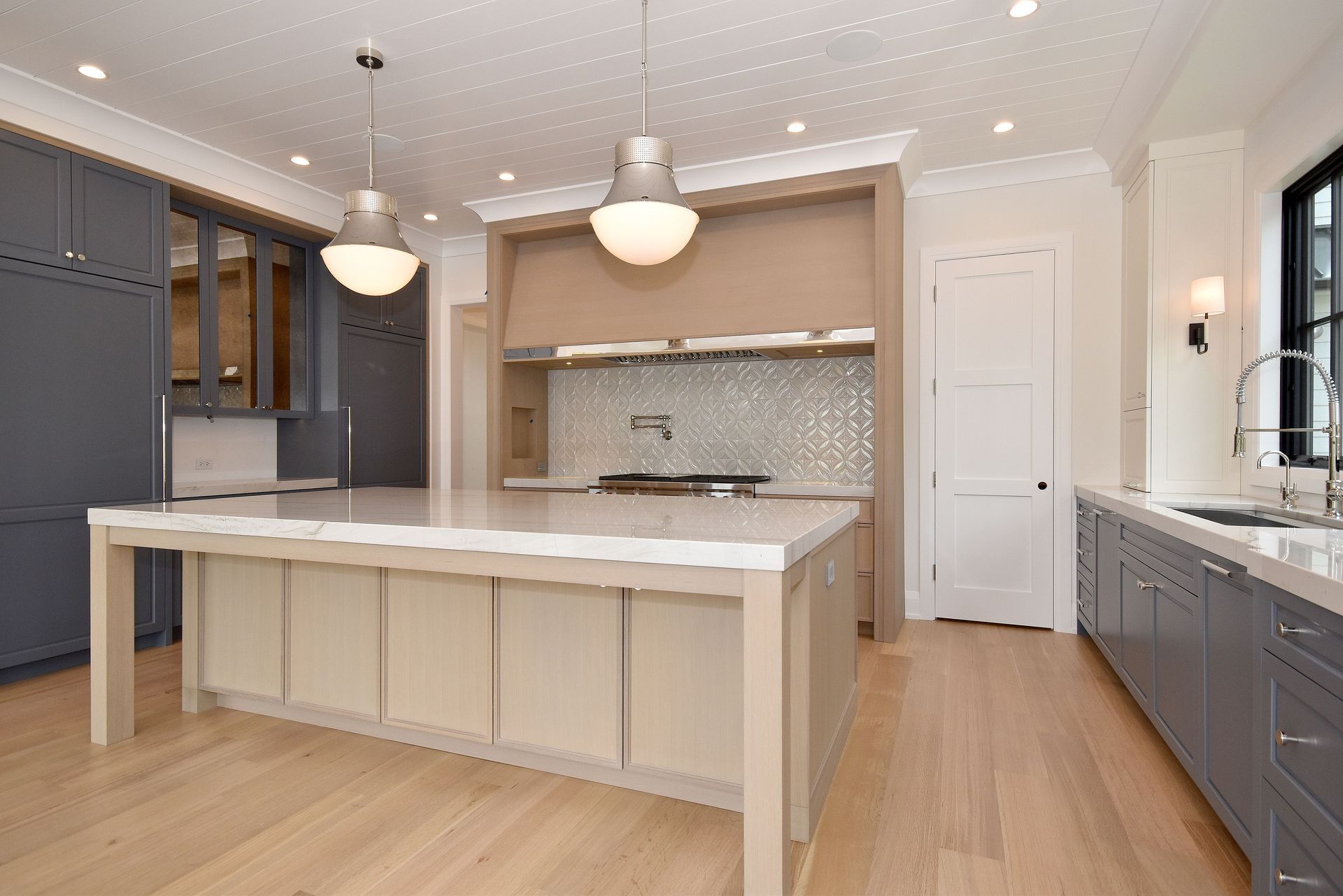 Bright modern kitchen with gray cabinets, white island, wood floors, and pendant lights