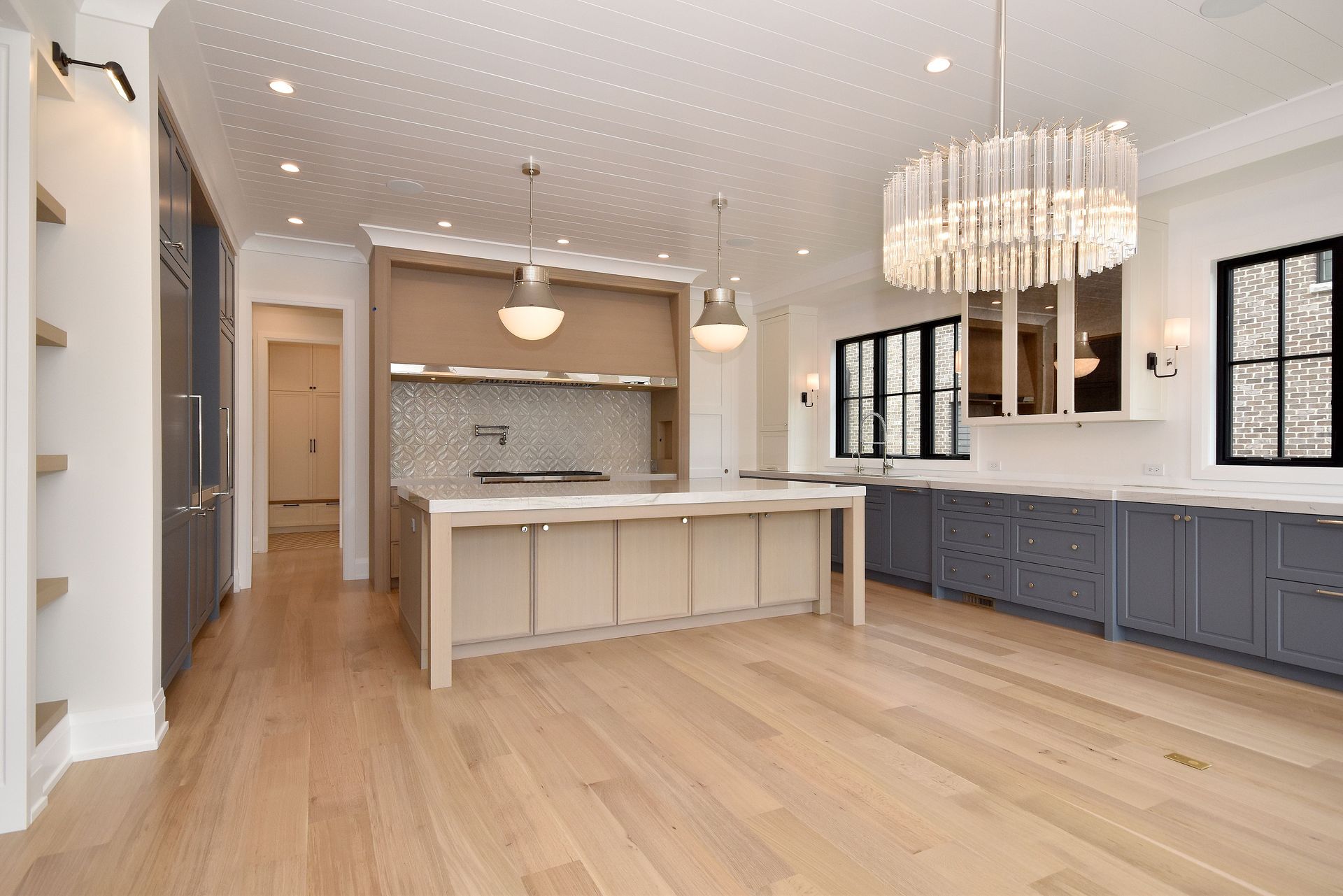 Bright modern kitchen with white island, gray cabinets, wood floors, and chandelier lighting