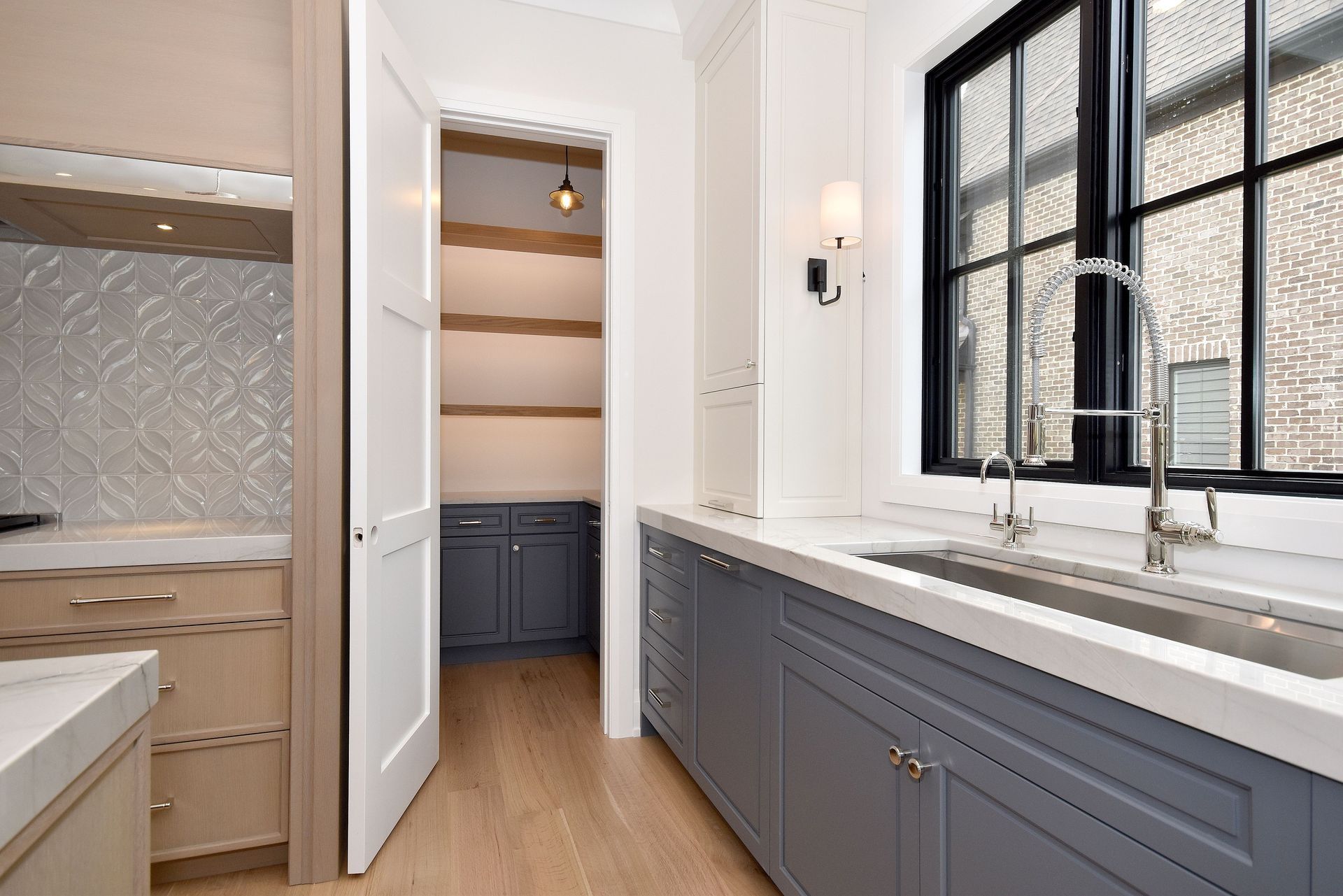Bright laundry room with gray cabinets, white countertops, open shelving, and a window by the sink.
