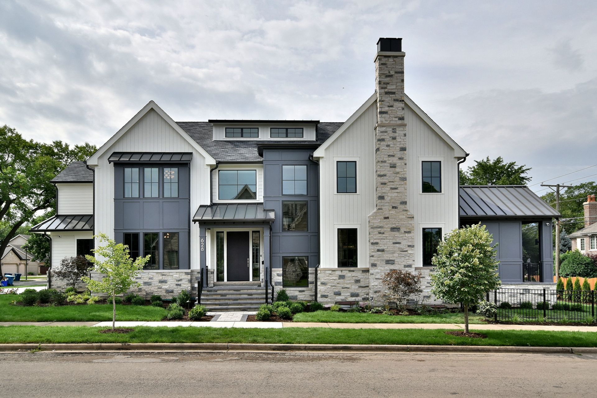 Modern two-story house with gray siding, stone chimney, and landscaped front yard