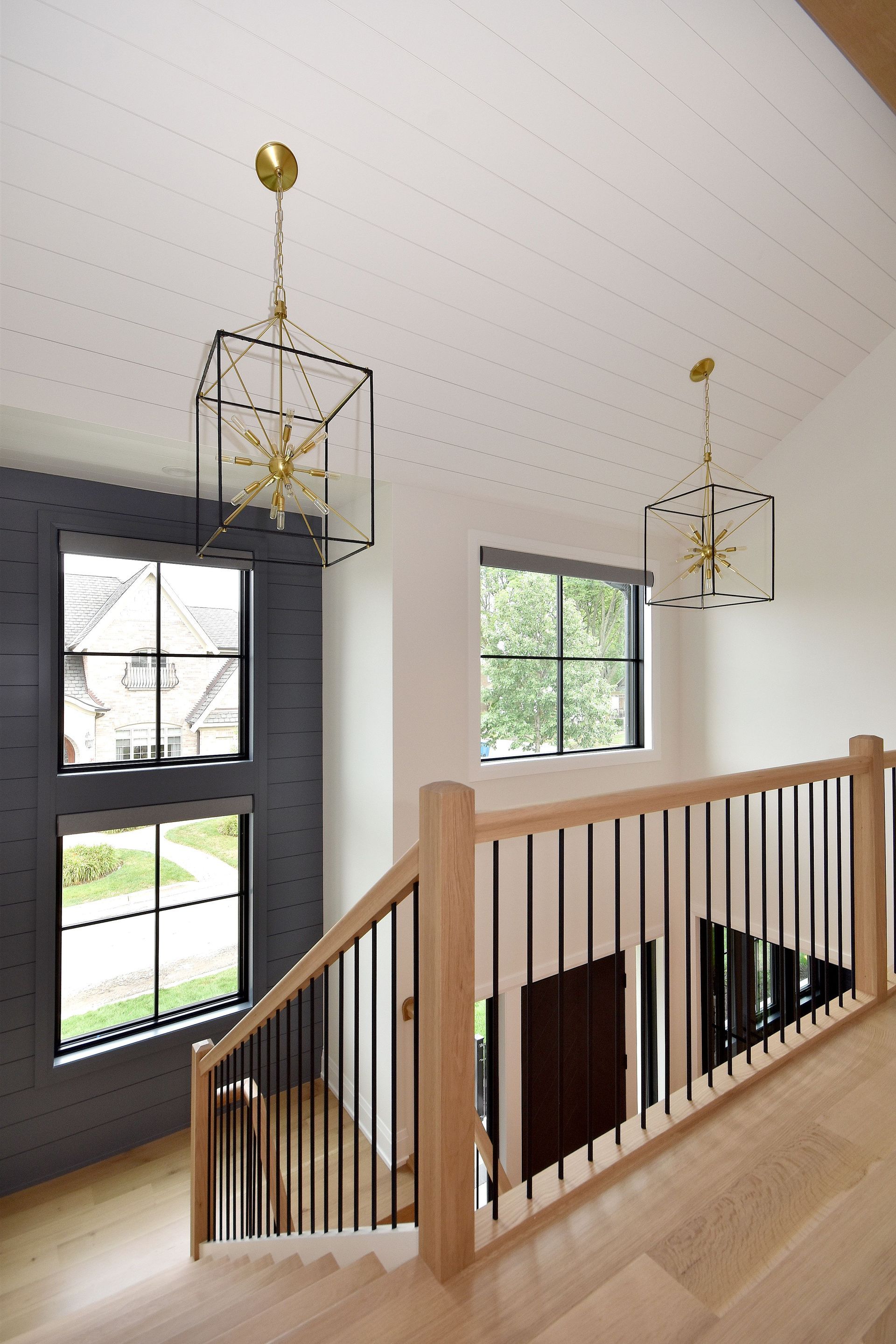 Modern stair landing with light wood railing, black-framed windows, and geometric pendant lights.