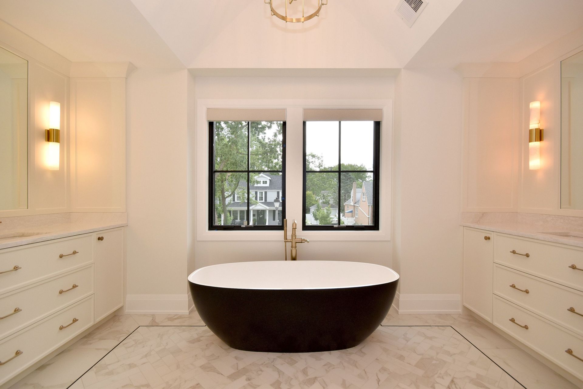 Bright modern bathroom with a freestanding oval tub, white cabinetry, and windows overlooking trees