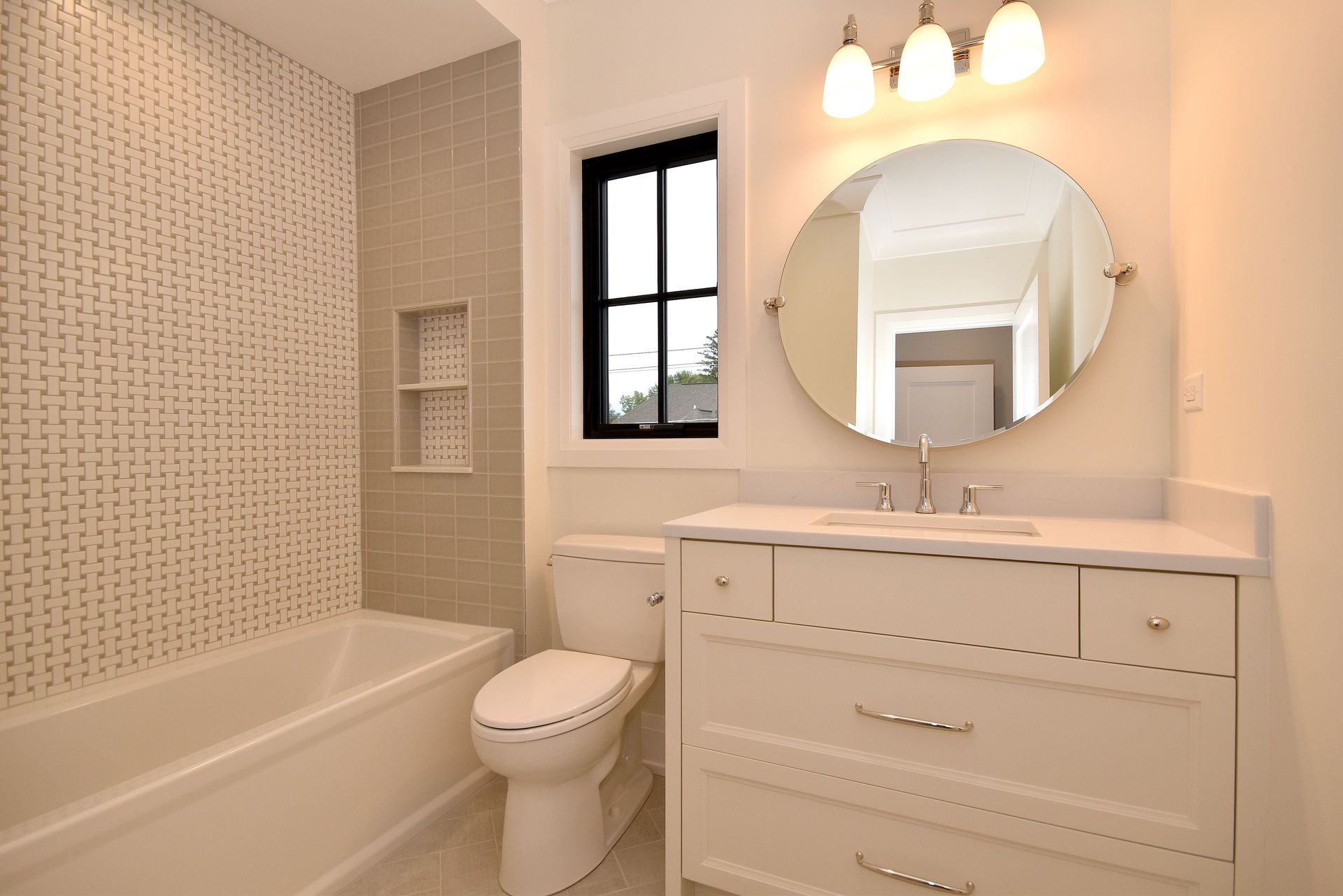 Bright bathroom with a tub, toilet, vanity, round mirror, and warm pendant lights