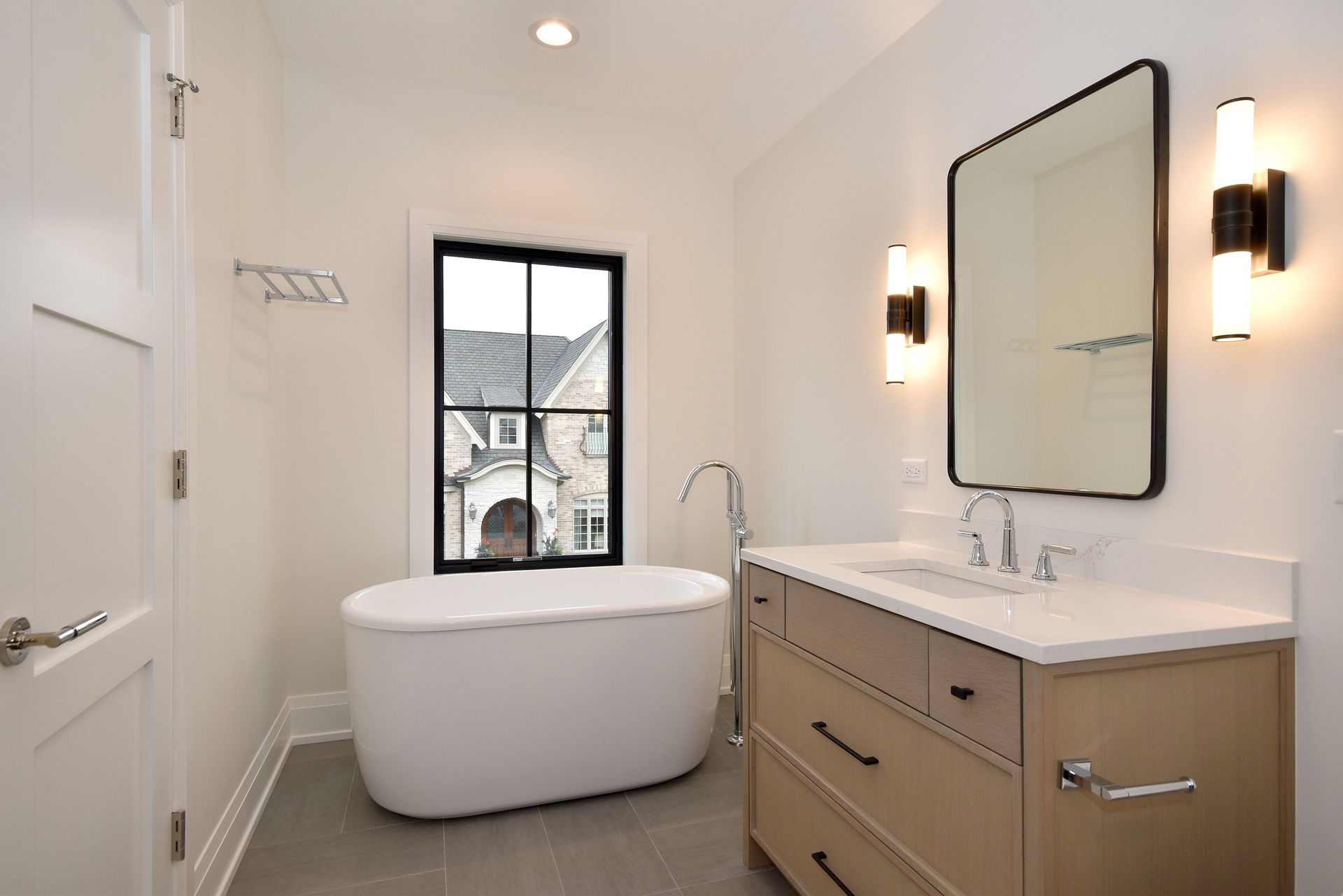 Modern bathroom with freestanding tub, vanity, mirror, and window overlooking houses