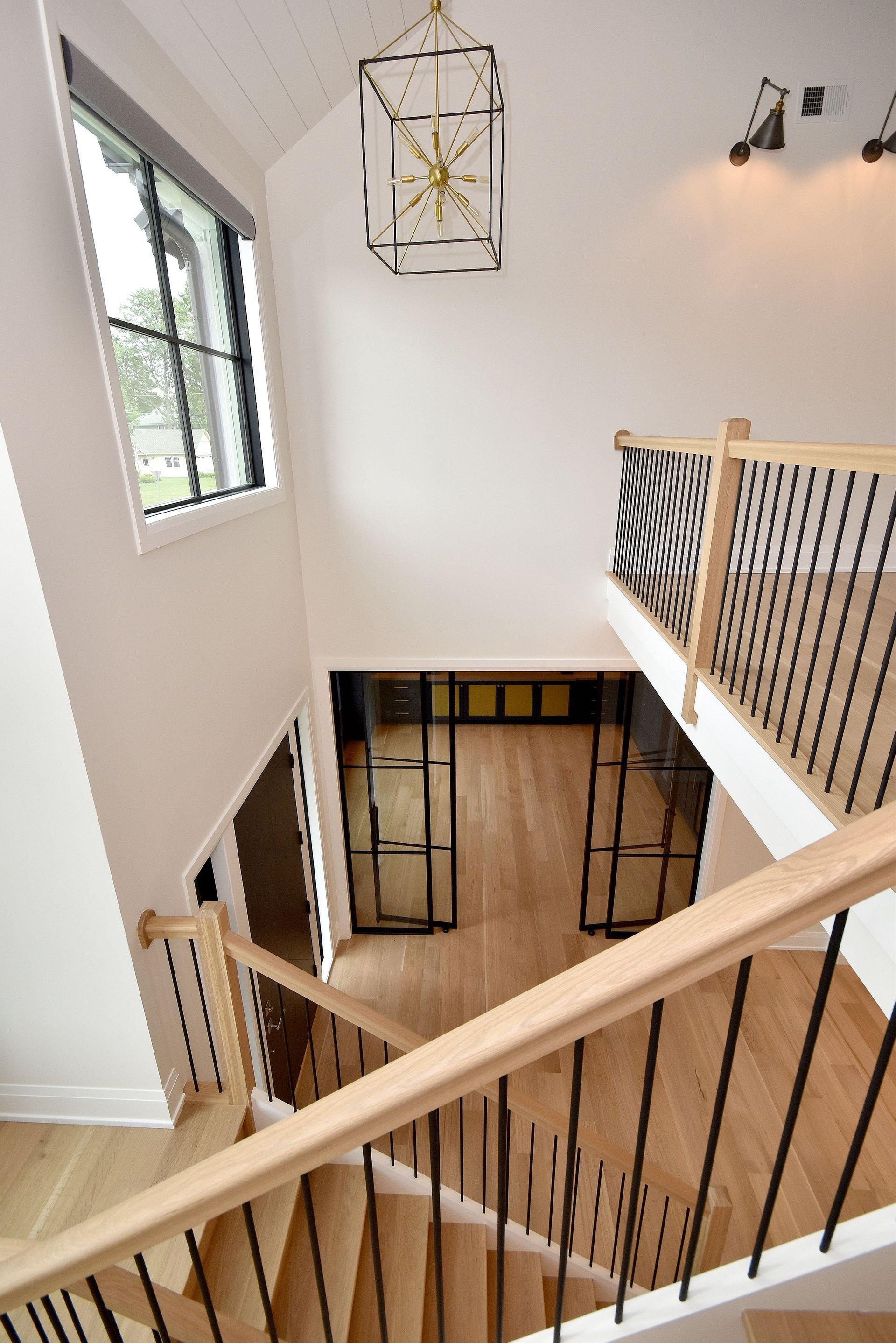 Staircase landing with white walls, wood floors, black railings, and large windows looking down into an entryway
