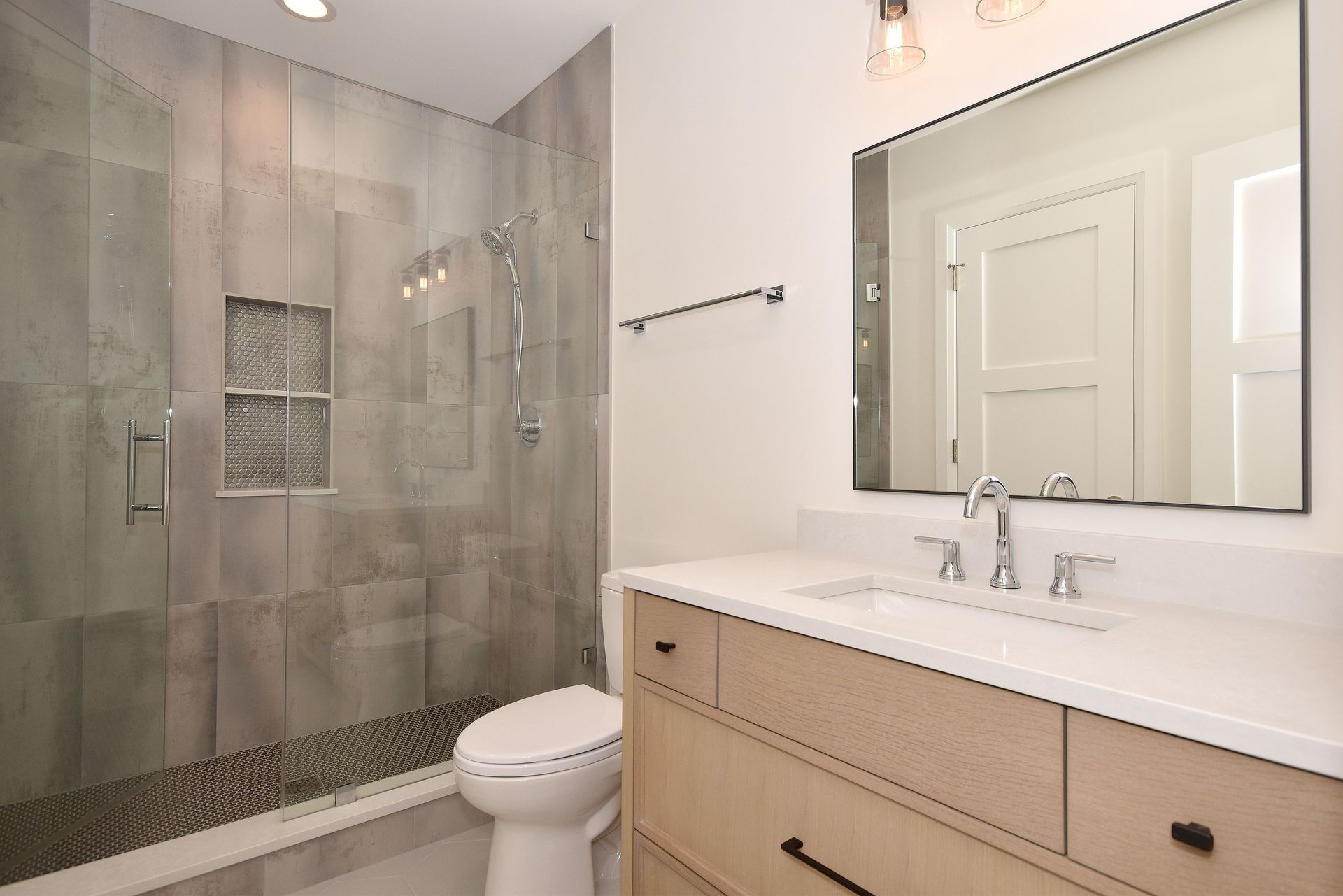 Modern bathroom with tiled walk-in shower, toilet, and wood vanity with mirror