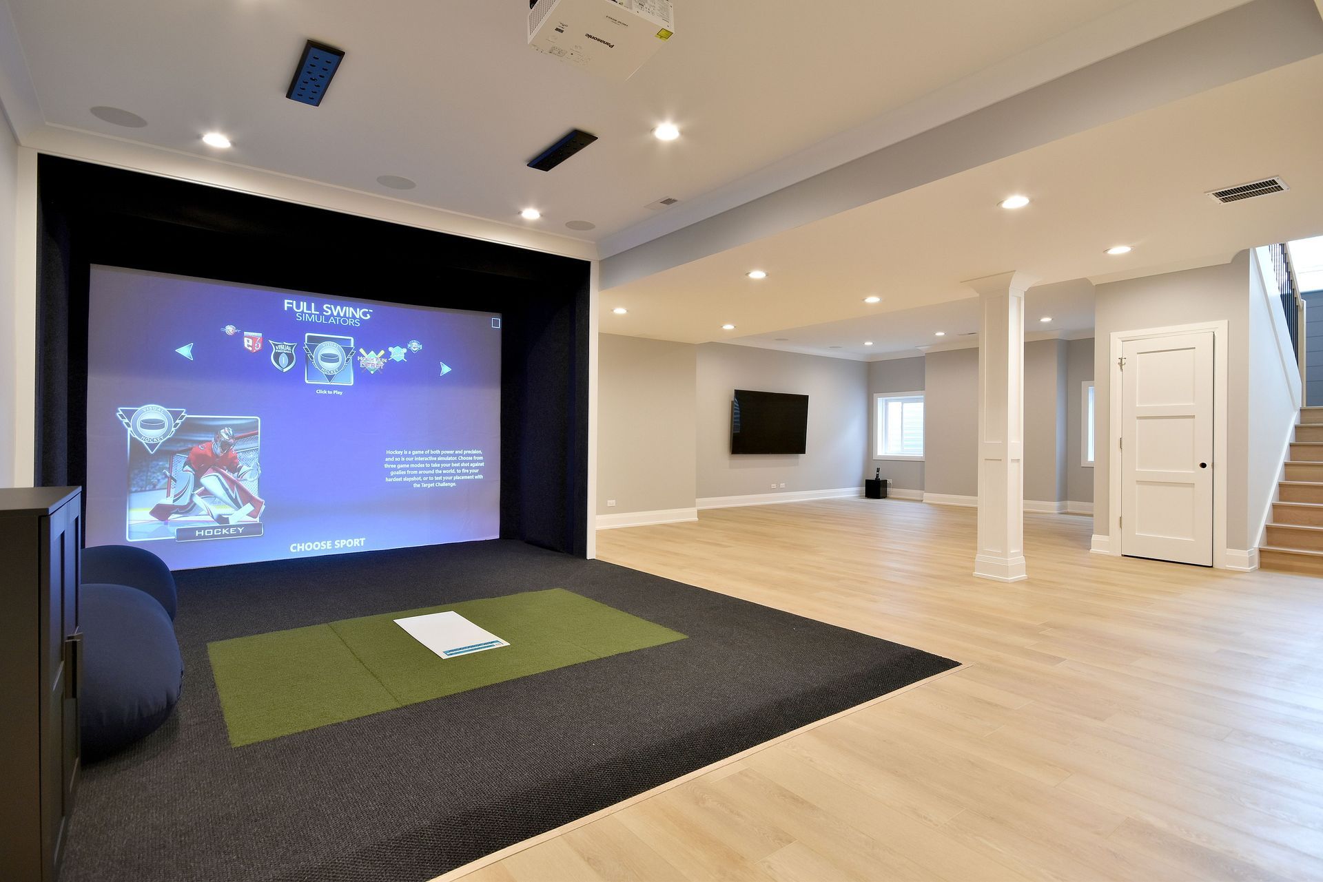 Spacious home theater with a large projector screen, black carpeted stage, and light wood flooring