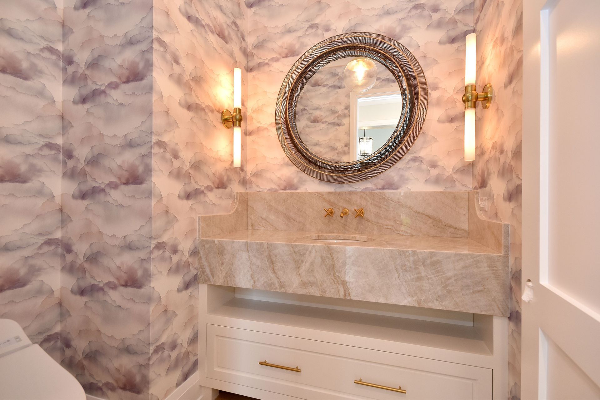 Elegant marble bathroom vanity with round mirror, wall sconces, and white cabinetry