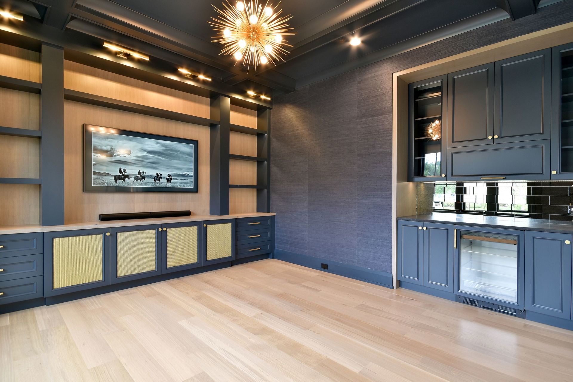 Modern living room with blue paneled walls, light wood floors, and a wall-mounted TV above built-in cabinets.