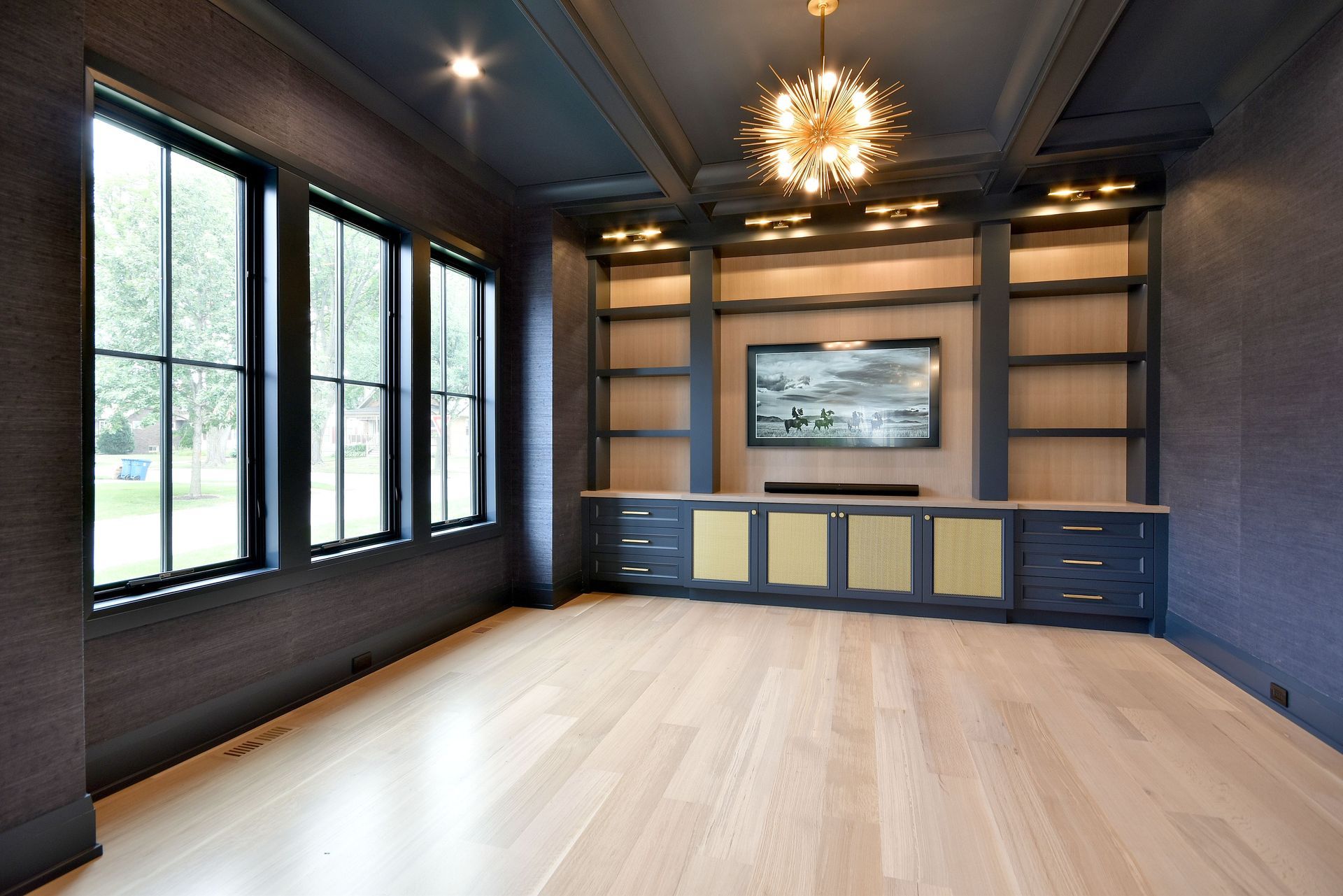 Modern empty living room with dark walls, large windows, light wood floor, and built-in TV wall