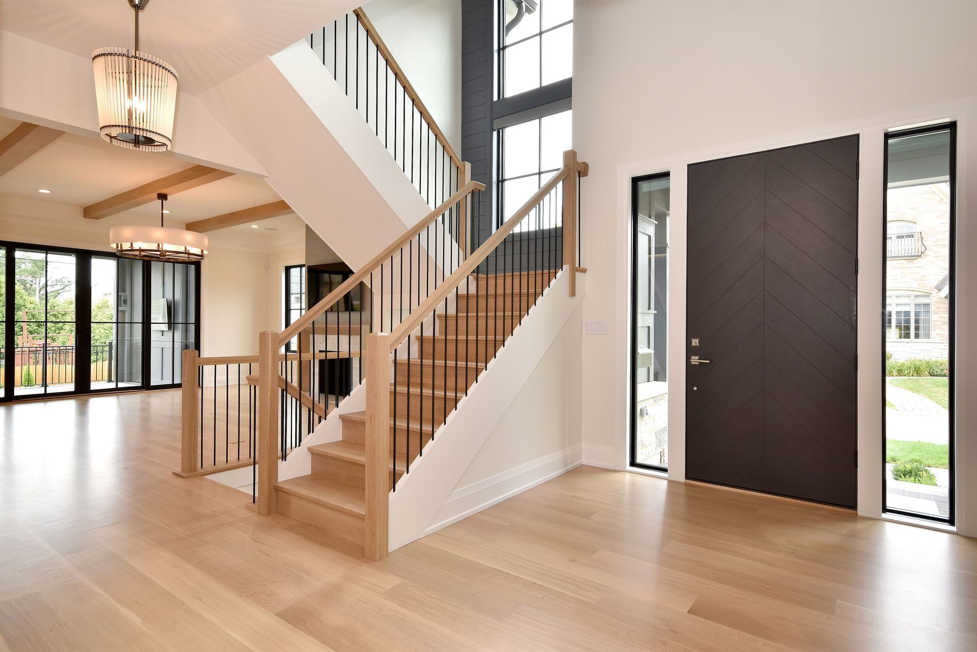 Bright modern entryway with wooden staircase, light hardwood floors, and tall black front door