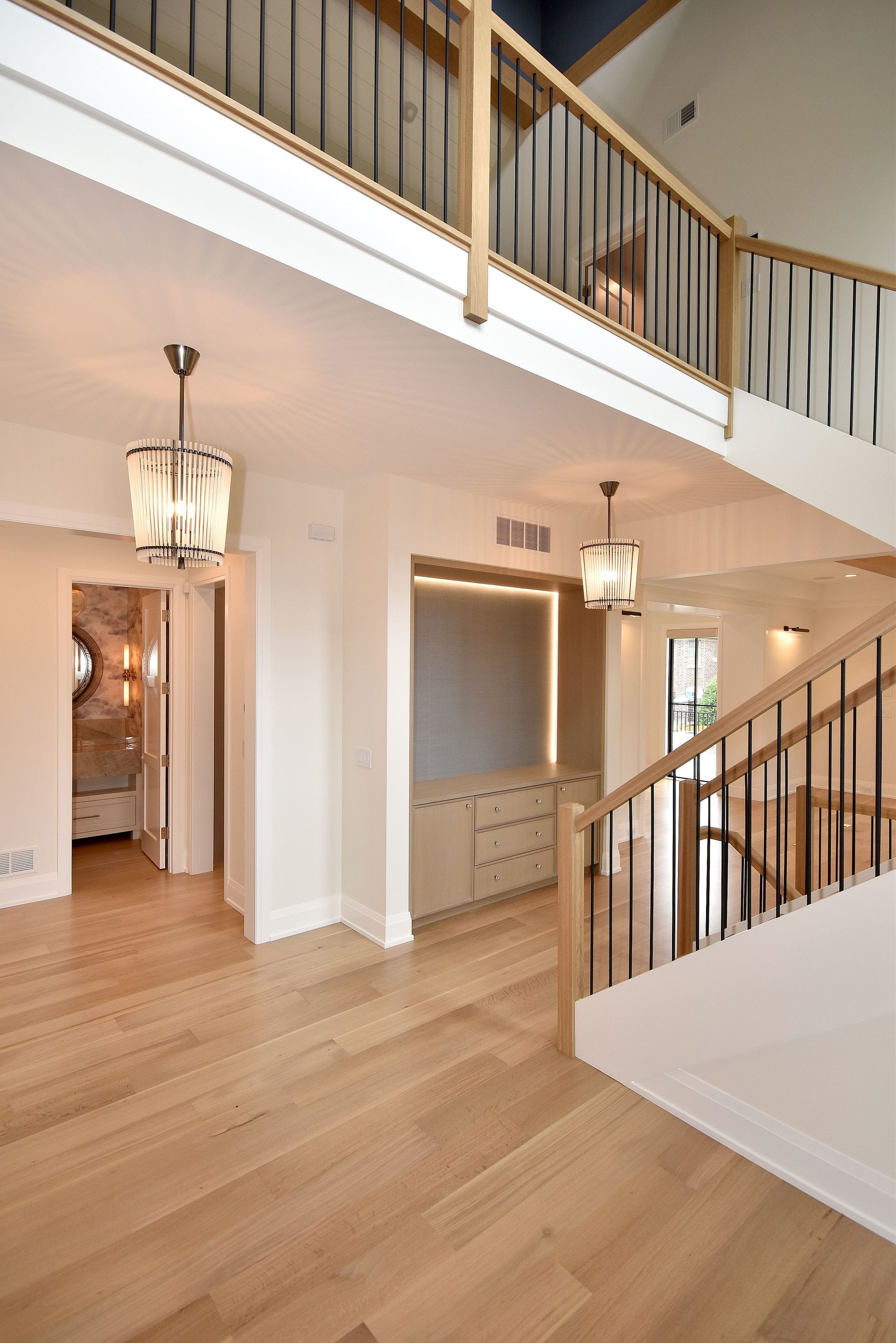 Bright two-story foyer with wood floors, chandeliers, white walls, and a staircase with wood railing.