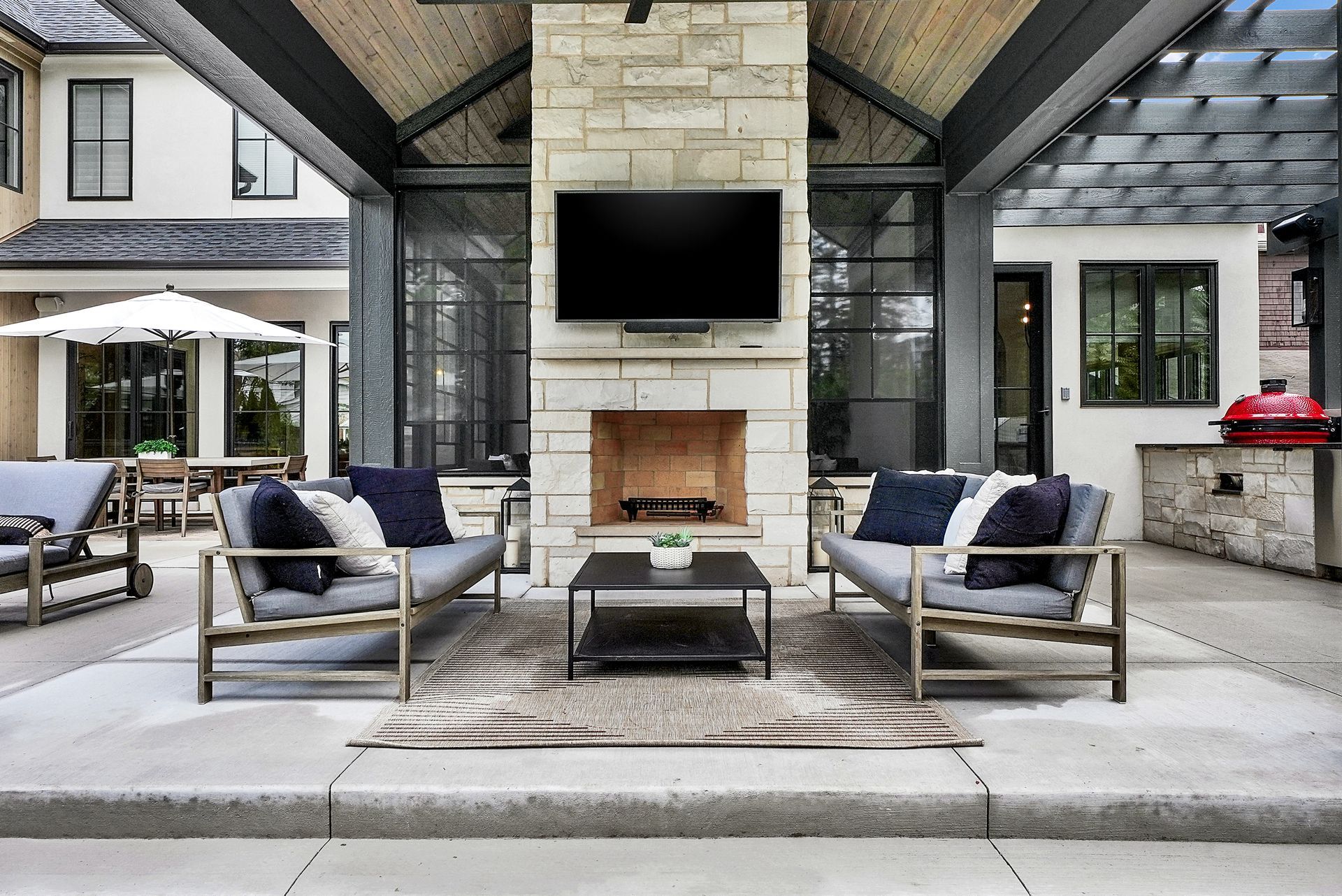 Covered patio with stone fireplace, wall-mounted TV, and gray seating around a coffee table