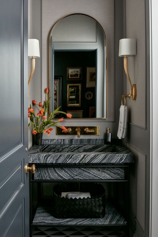Elegant hallway vanity with marble table, arched mirror, wall sconces, and a small floral arrangement