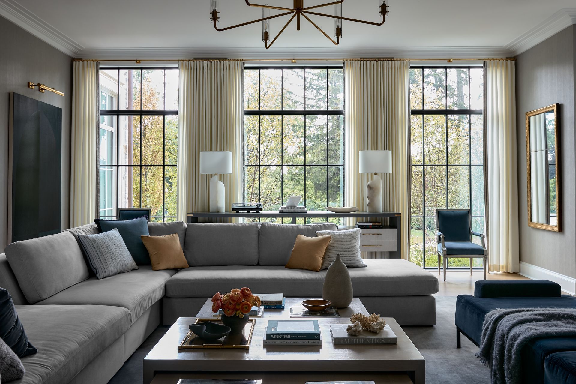 Modern living room with large windows, gray sectional, coffee table, and blue armchair