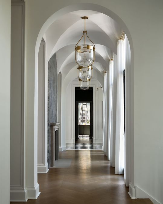 Elegant hallway with white arched ceilings, hanging chandeliers, and hardwood floors.