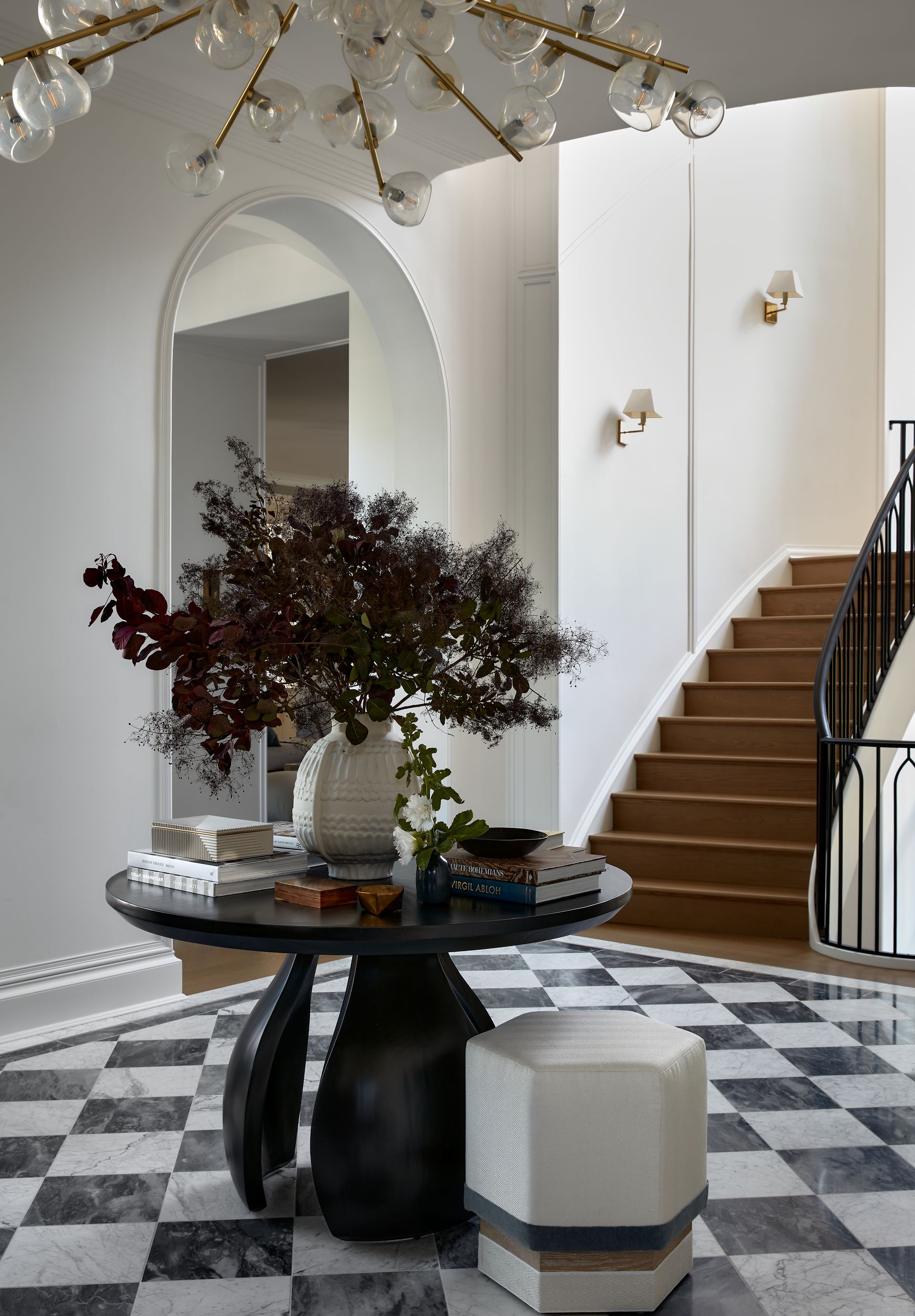 Elegant lobby with arched walls, a staircase, black-and-white floor, and a round table with flowers.