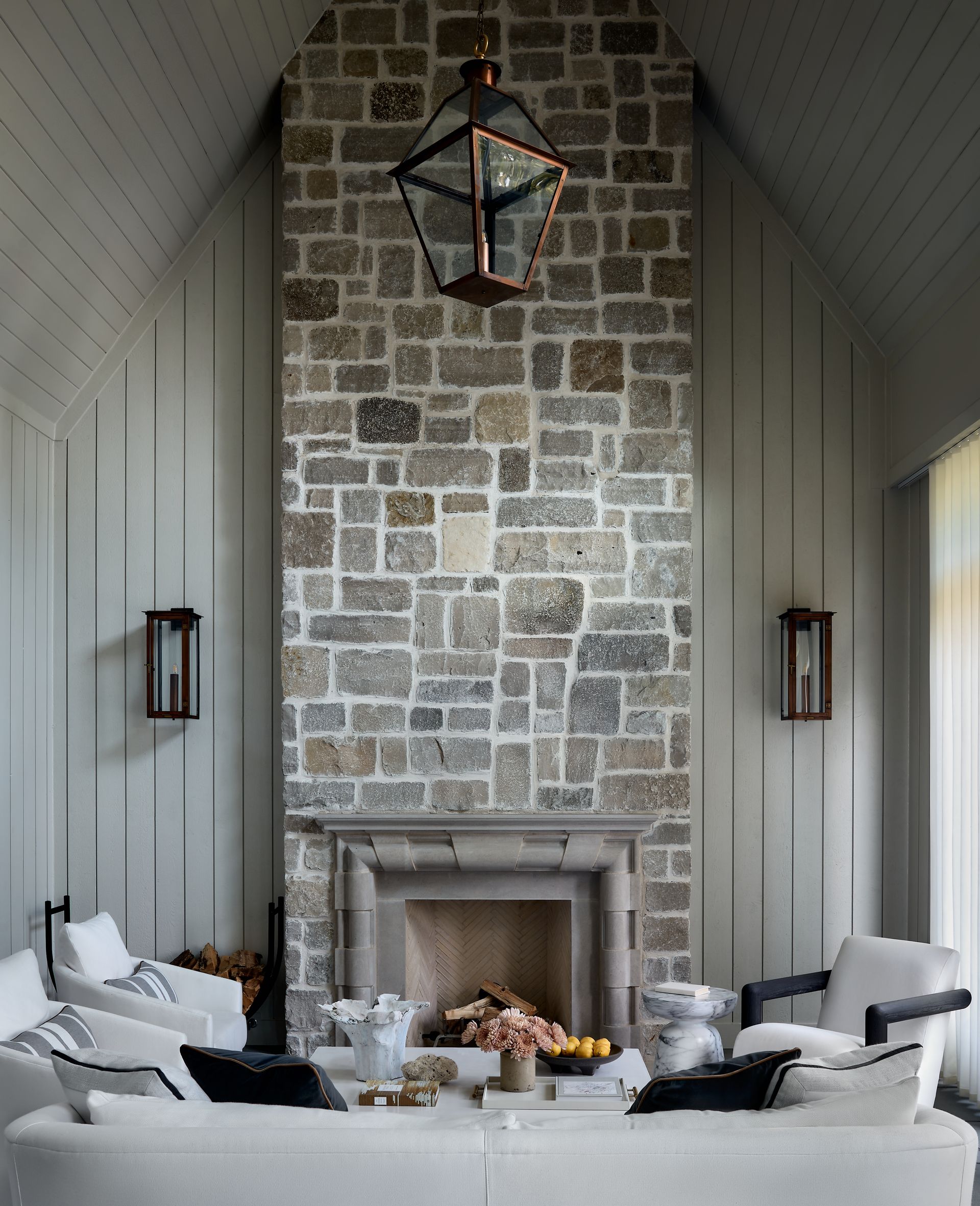 Stone fireplace in a cozy, vaulted living room with white chairs and a black lantern light fixture.