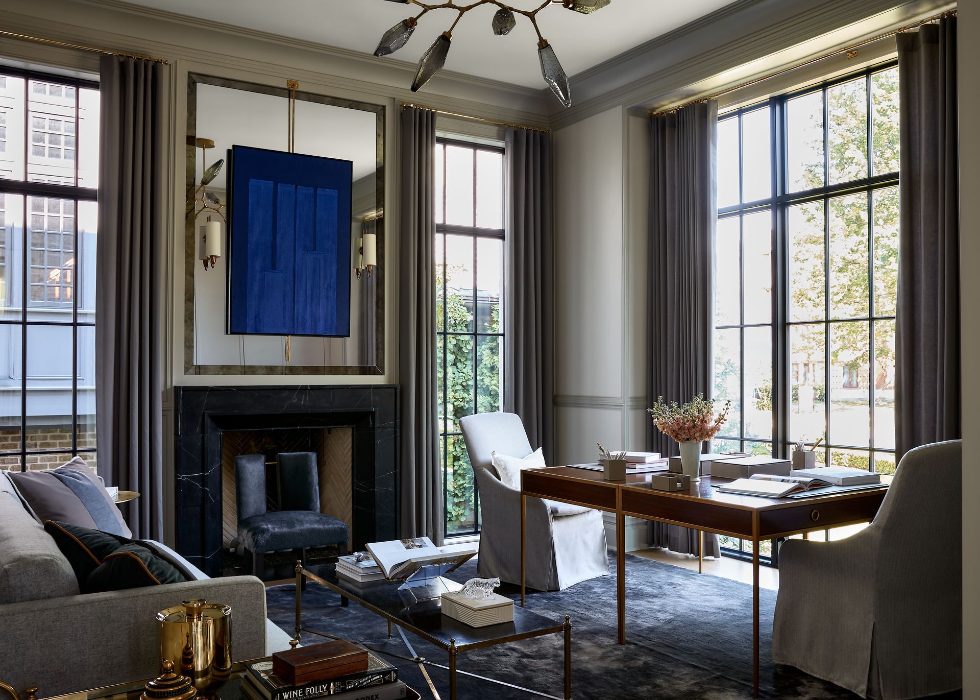 Elegant living room with fireplace, large windows, and dining table set beneath a blue wall art piece
