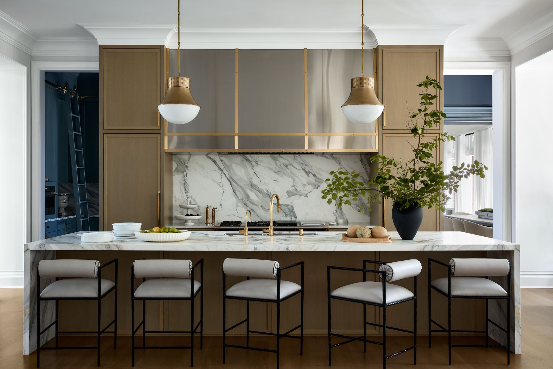 Modern kitchen with marble island, gold accents, pendant lights, and four stools
