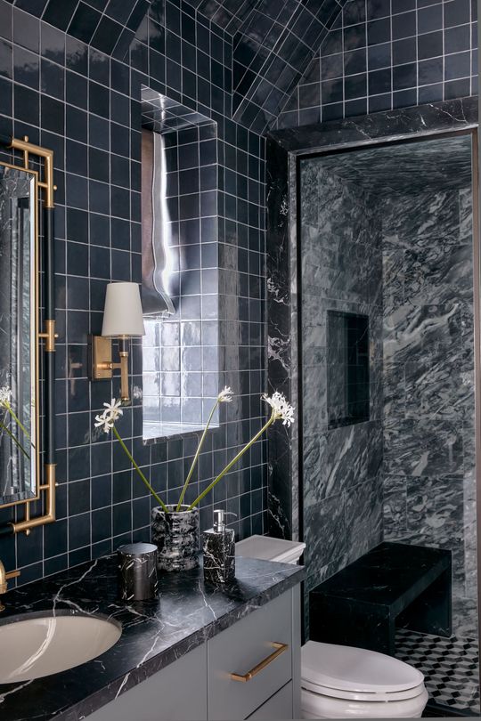 Elegant black-tiled bathroom with marble shower, sink vanity, and white toilet