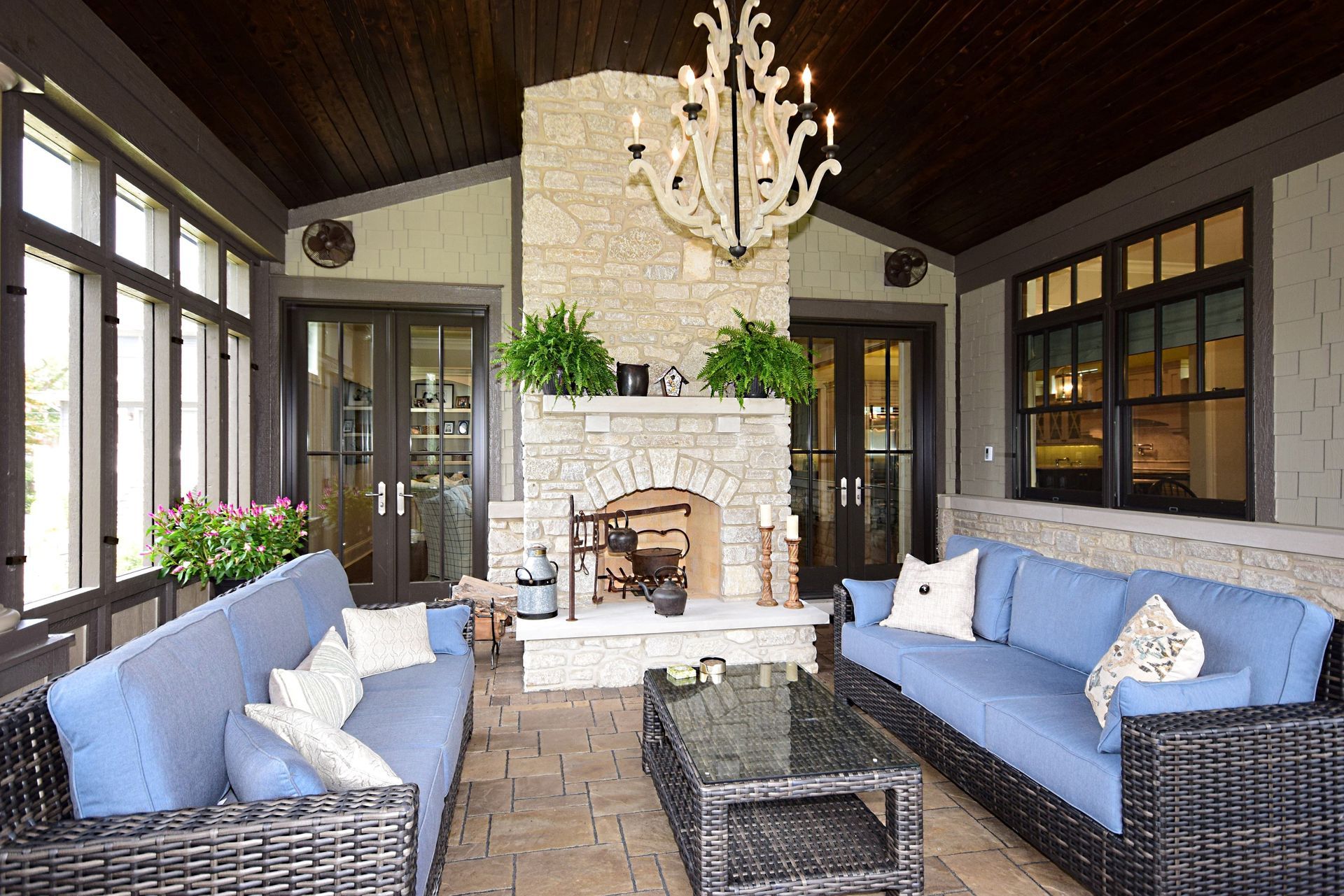 Outdoor screened porch with wicker sofas, blue cushions, stone fireplace, and chandelier