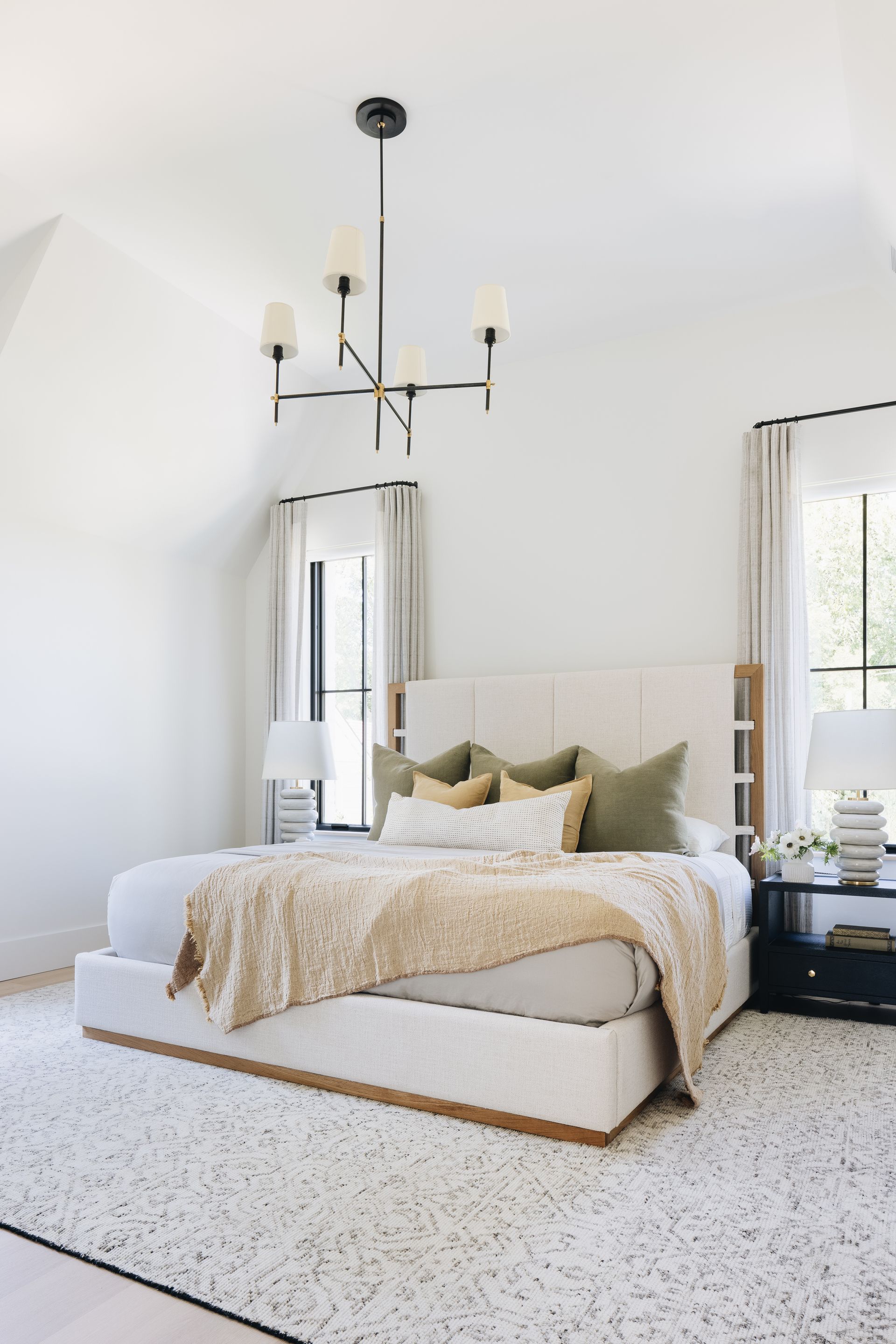 Bright minimalist bedroom with a bed, light curtains, black chandelier, and textured rug