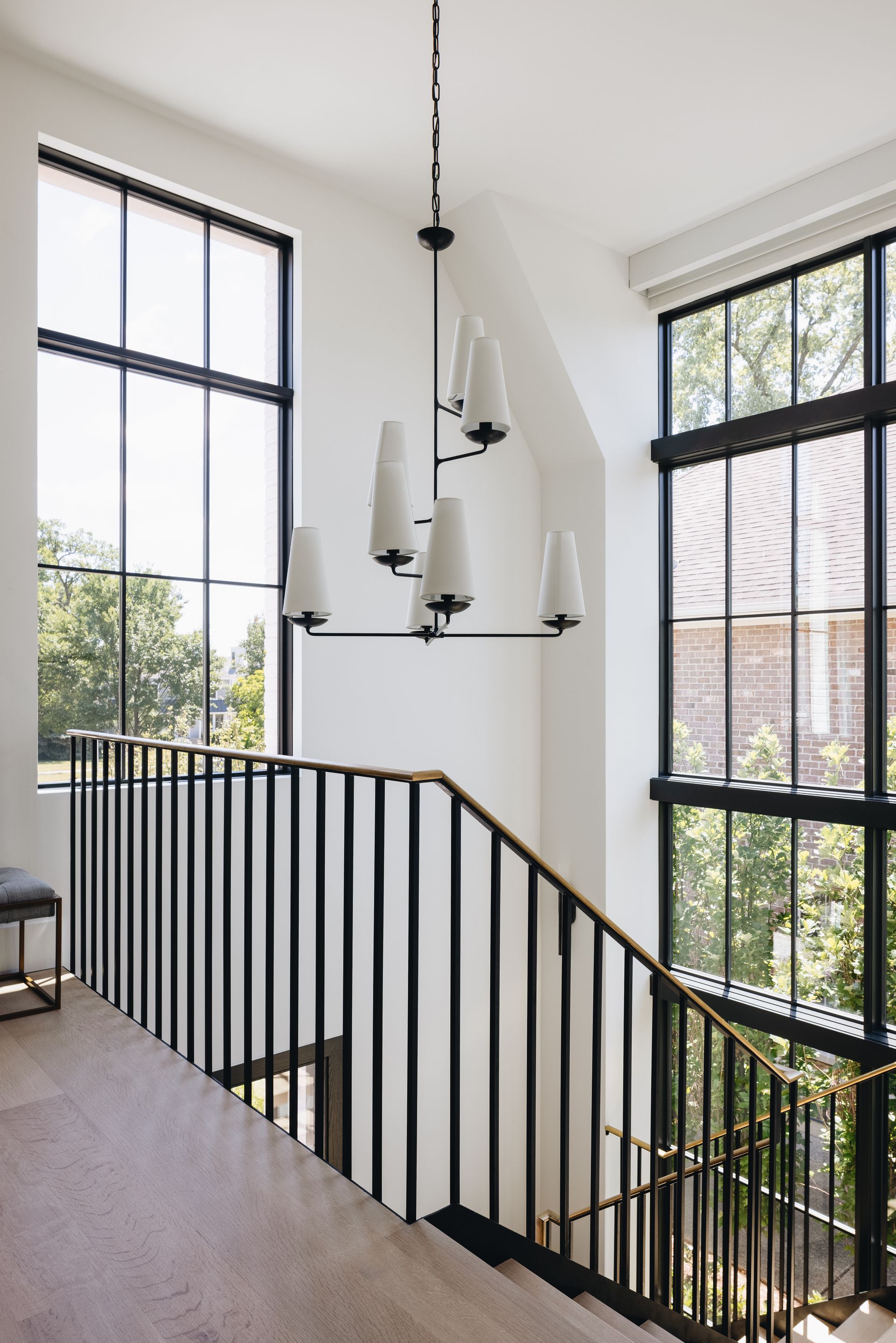 Modern staircase with black railing, pendant light, and tall windows in a bright interior.
