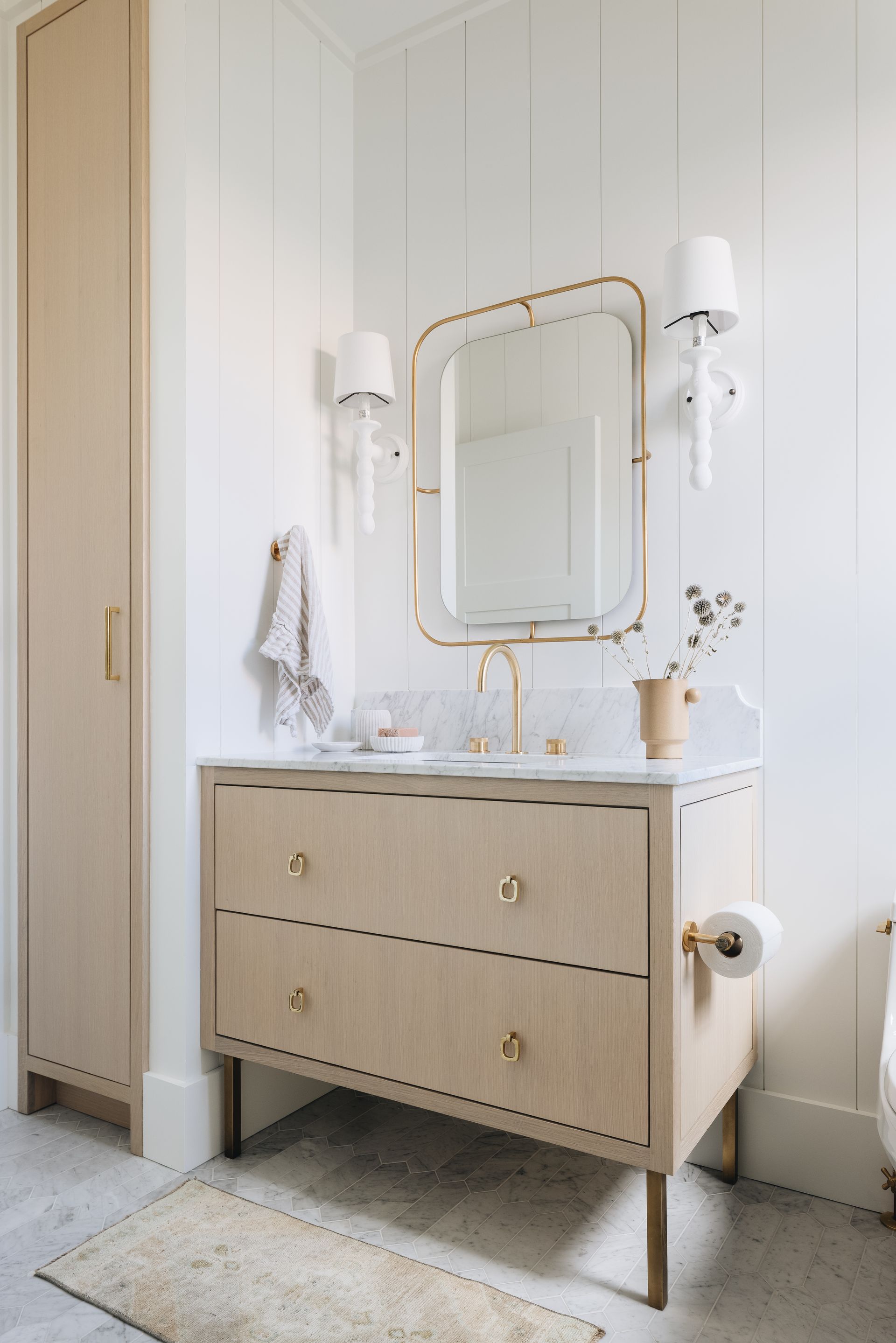 Elegant vanity table with mirror, sconces, and woven-front drawers in a bright cream room