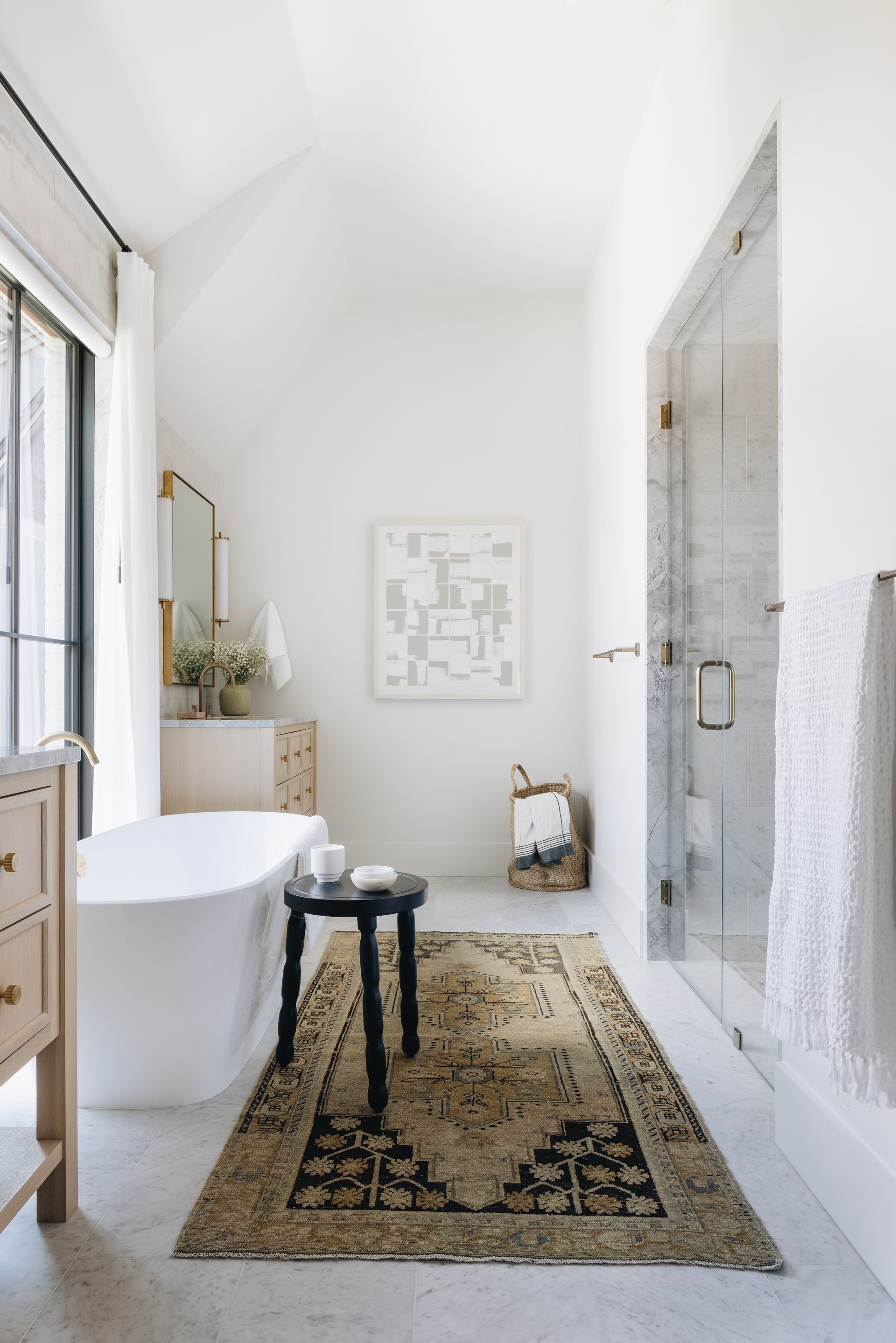 Bright minimalist bathroom with a bathtub, glass shower, woven rug, and small stool