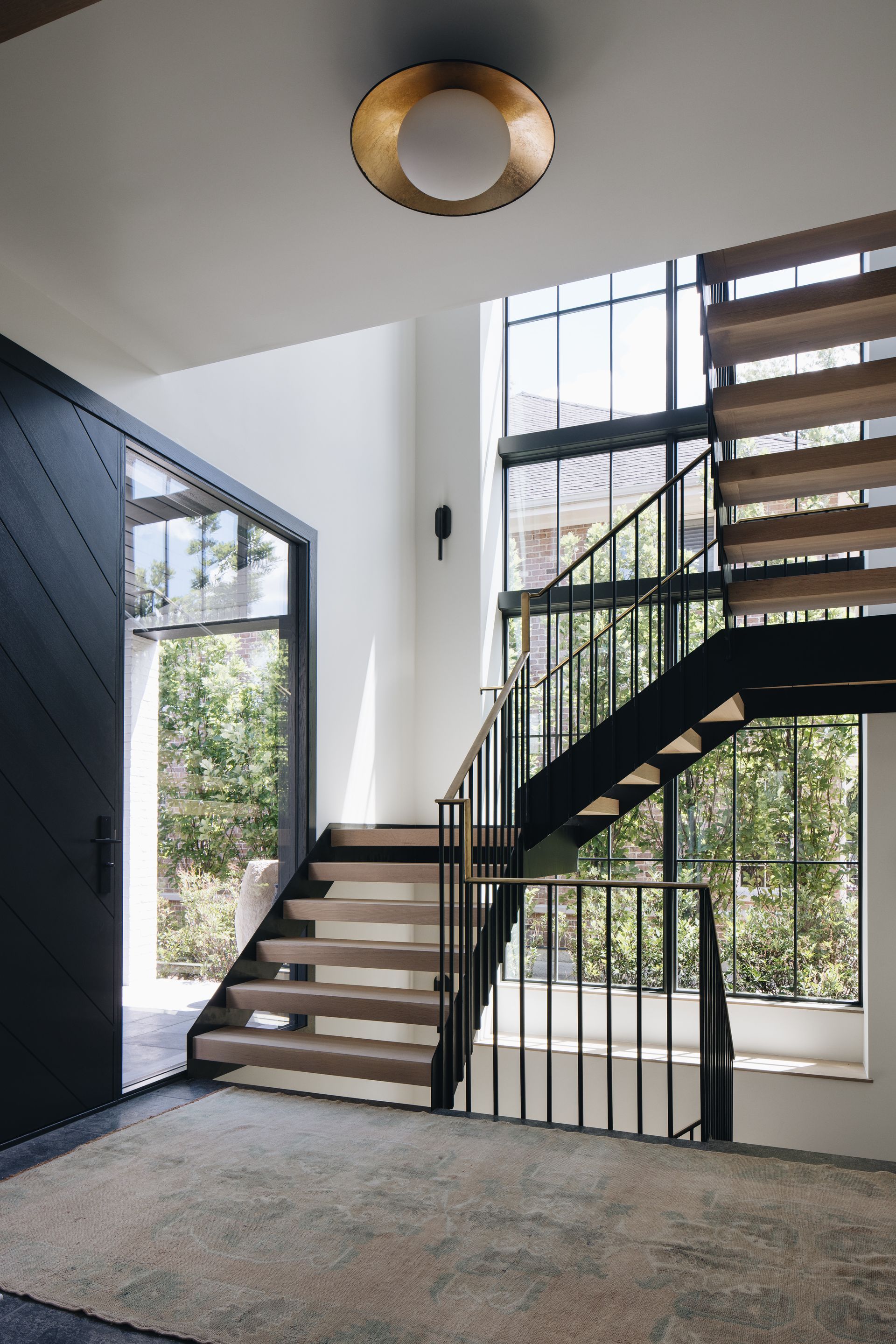 Modern stairwell with black railing, light wood steps, and large windows letting in natural light.