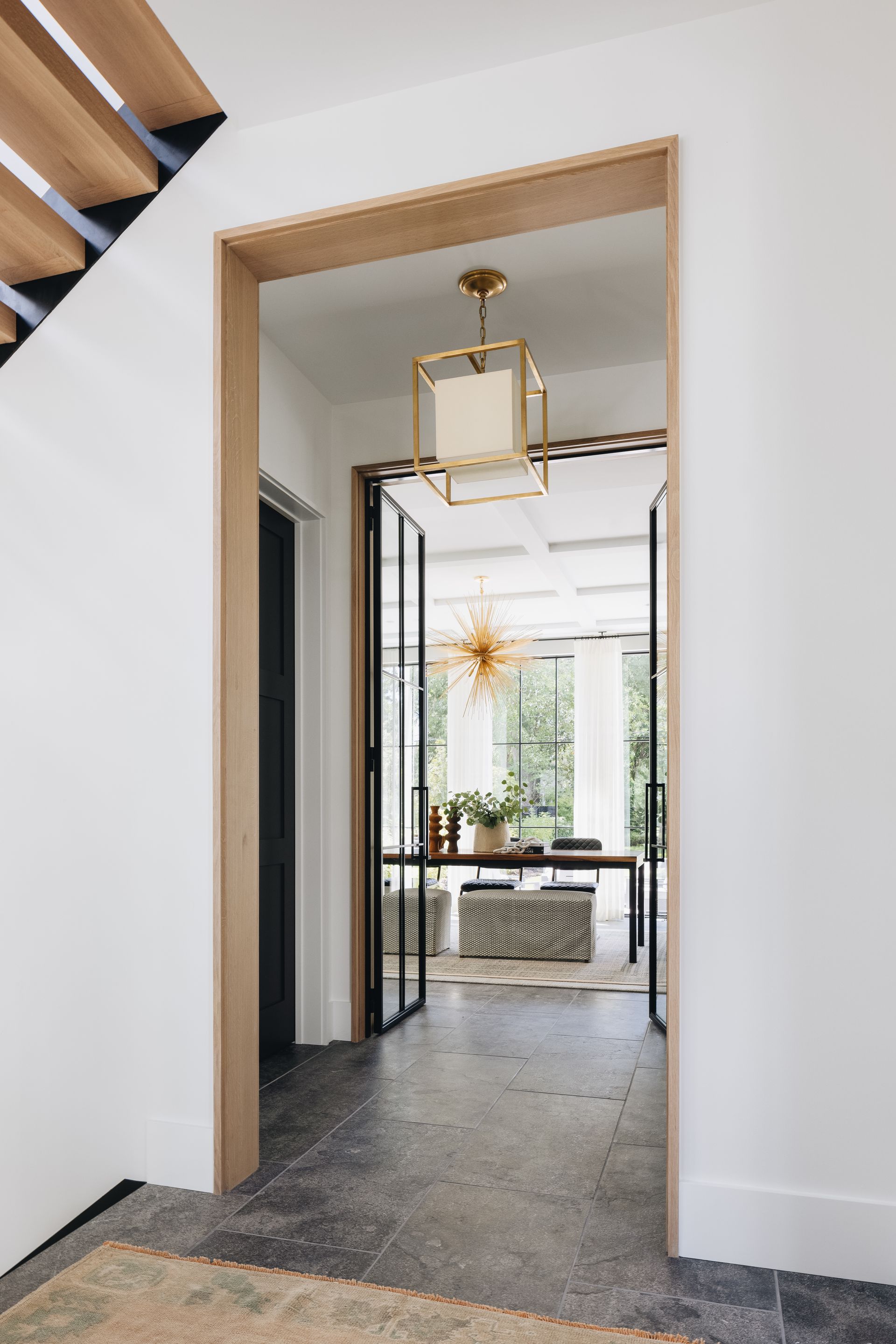 Modern hallway with wood-trimmed doorway opening to a bright room with glass doors and a hanging light fixture