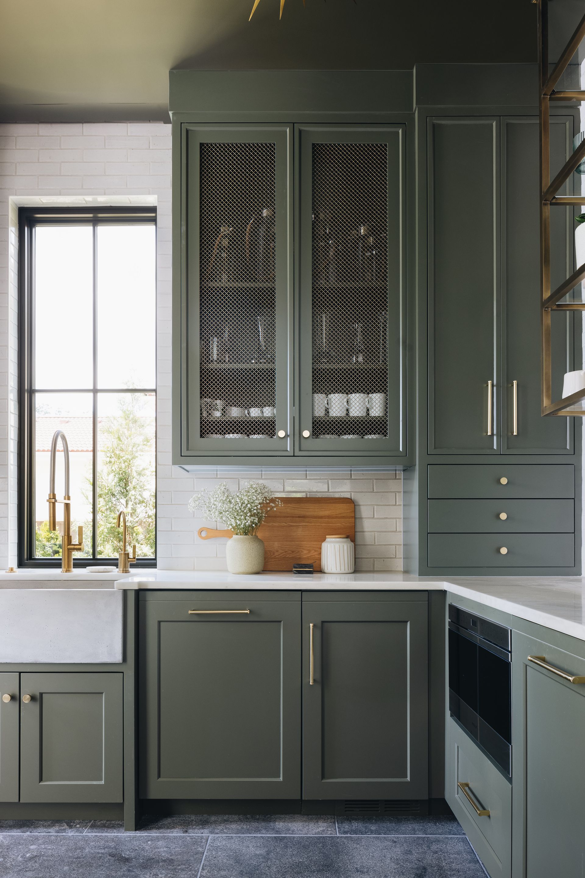 Modern green kitchen with glass-front cabinets, white counters, and a window over the sink.