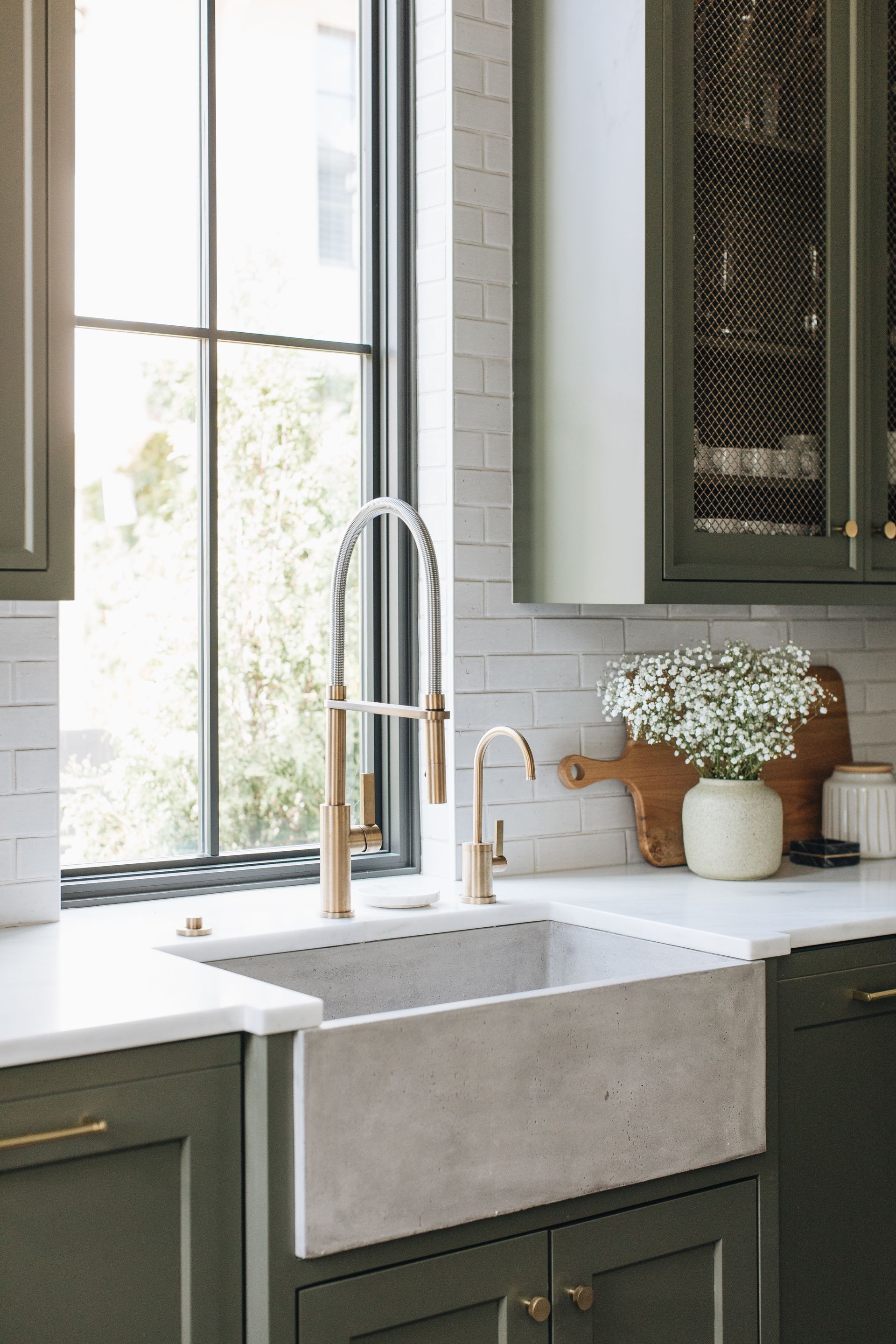 Modern kitchen sink with tall chrome faucet, white countertops, and a vase of flowers by a bright window