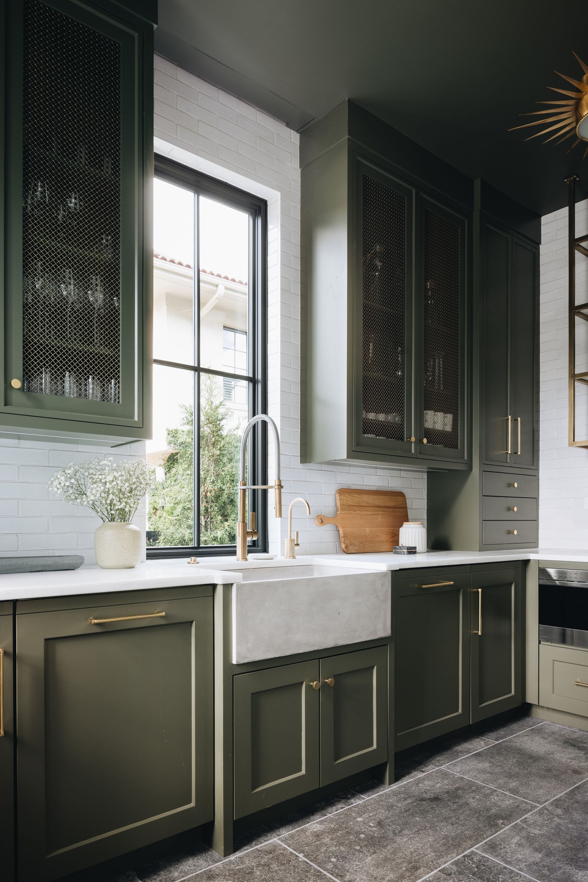 Dark green kitchen with white countertops, black cabinets, a window over the sink, and patterned cabinet fronts