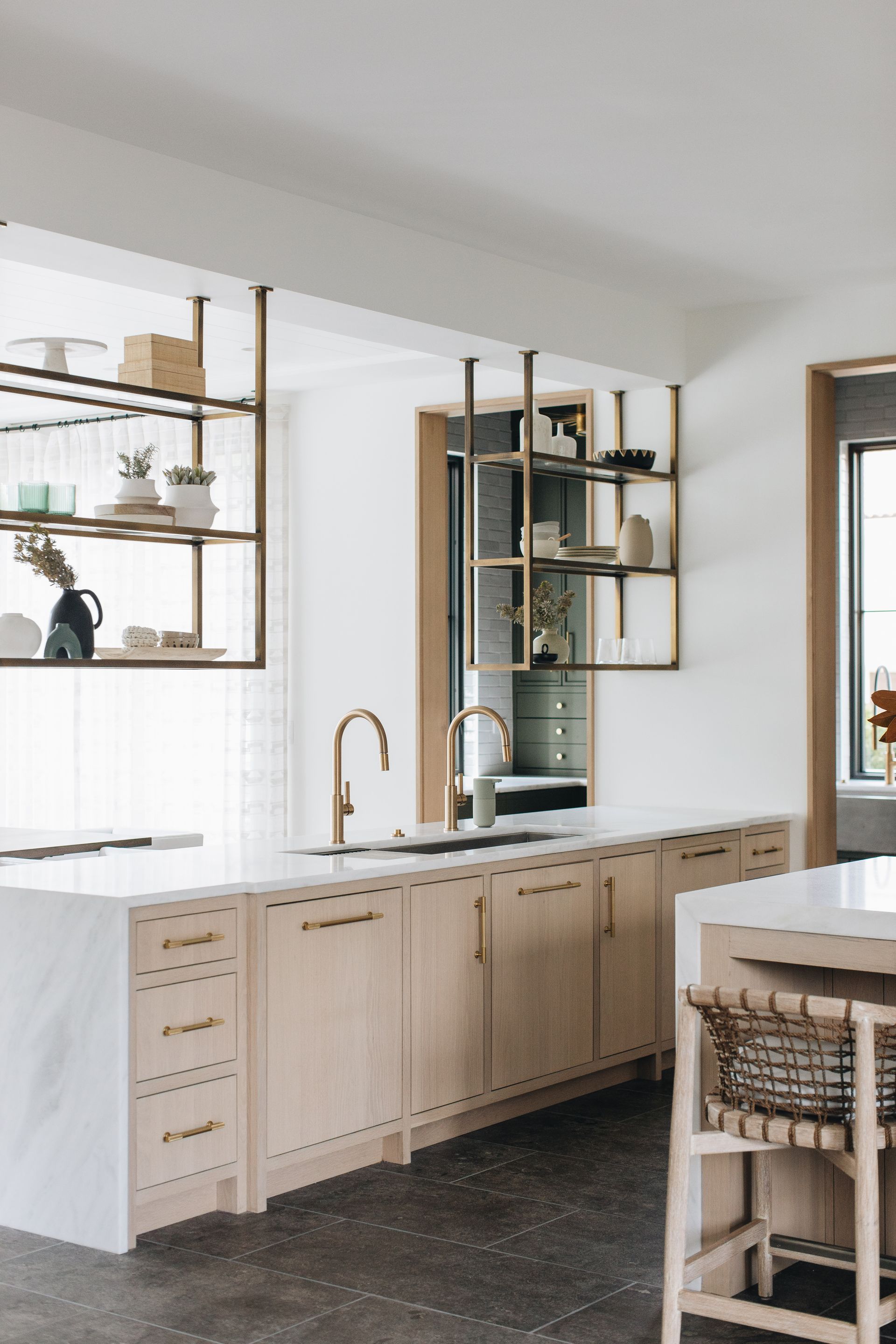 Bright modern kitchen with light wood cabinets, open shelving, and a large island near a window.