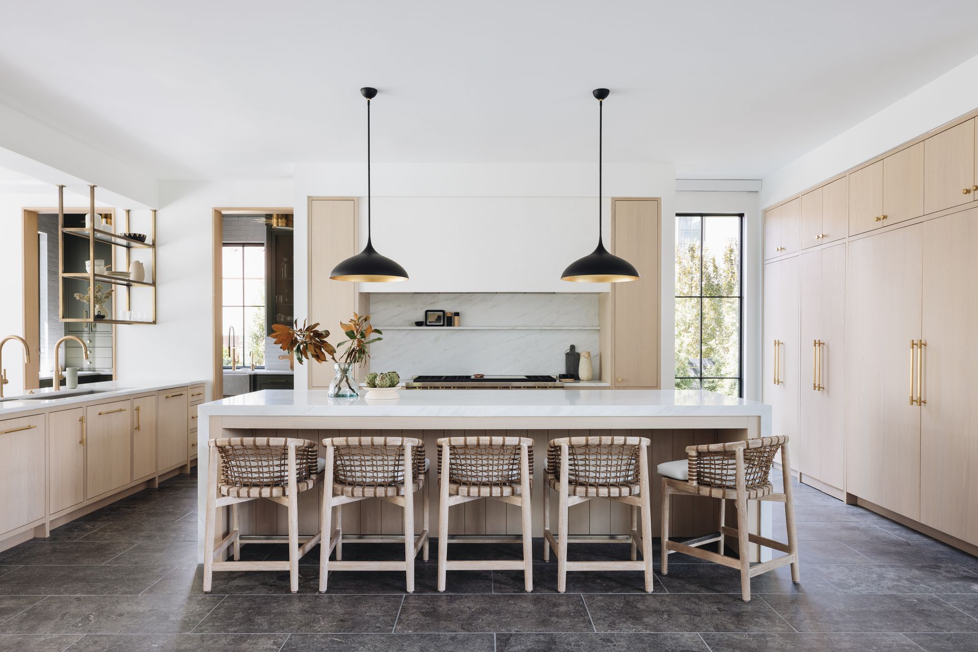 Modern white kitchen with a large island, bar stools, black pendant lights, and built-in cabinets