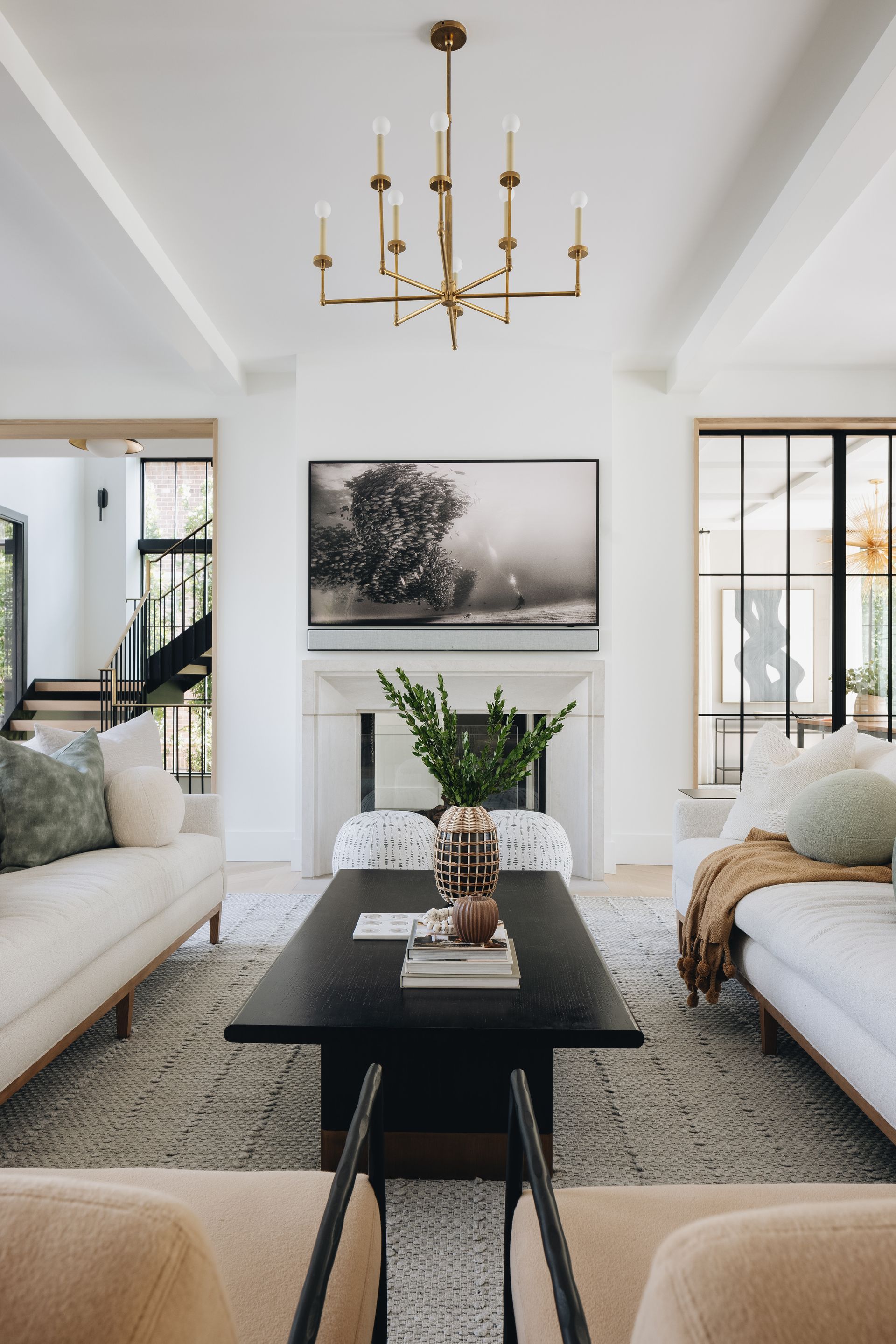 Bright living room with chandelier, white sofas, black coffee table, and large wall art.