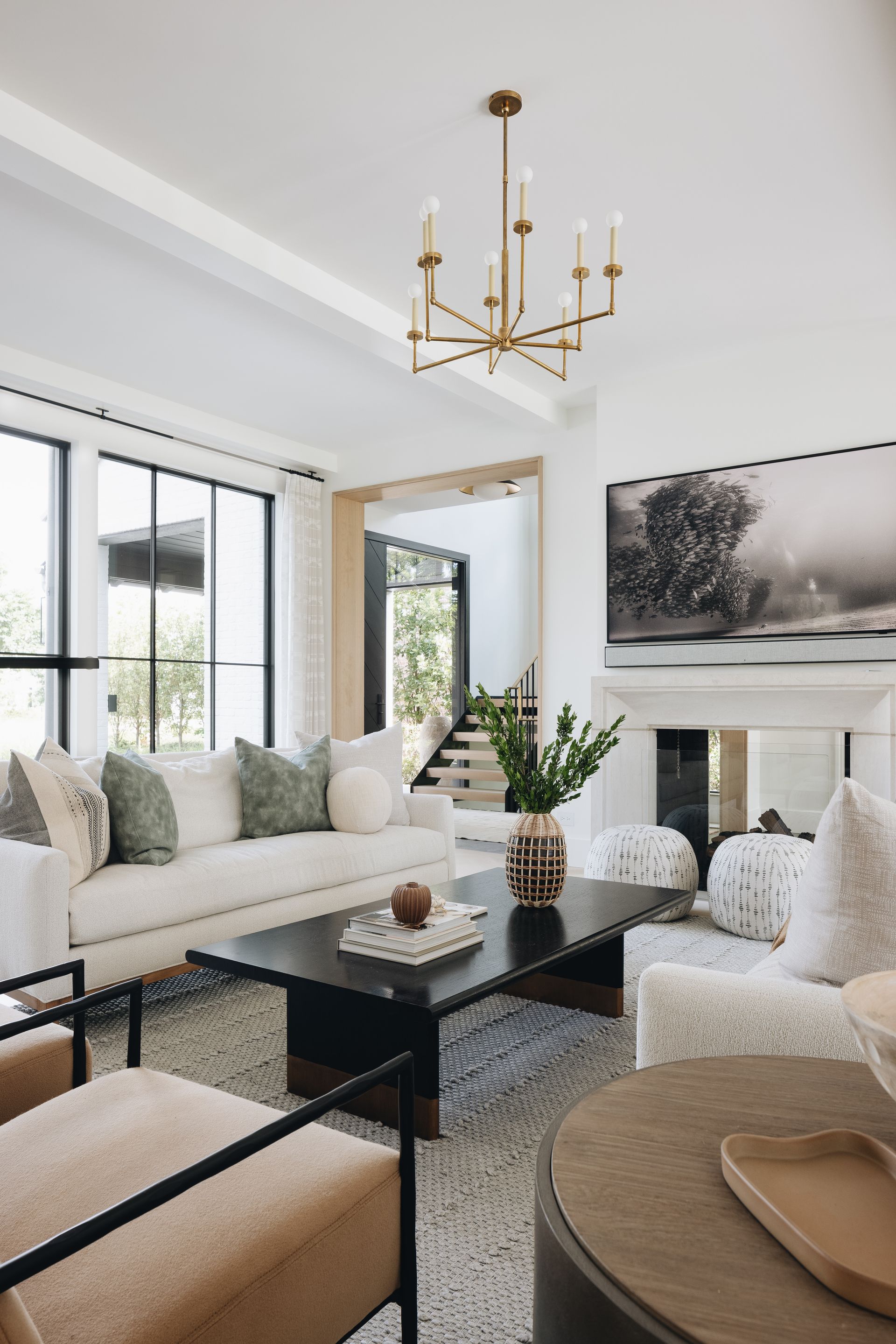 Bright modern living room with white sofas, black coffee table, gold chandelier, and large windows