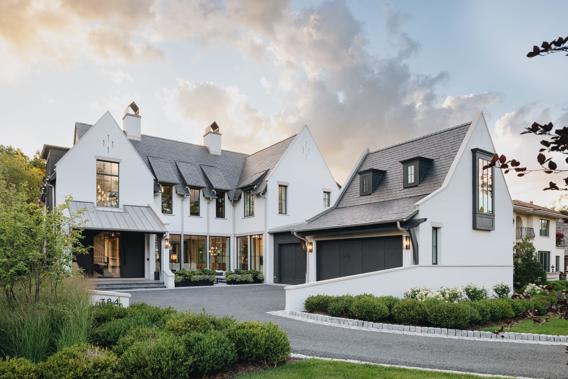 Modern white house with steep gabled roofs, large windows, and a landscaped front yard at dusk