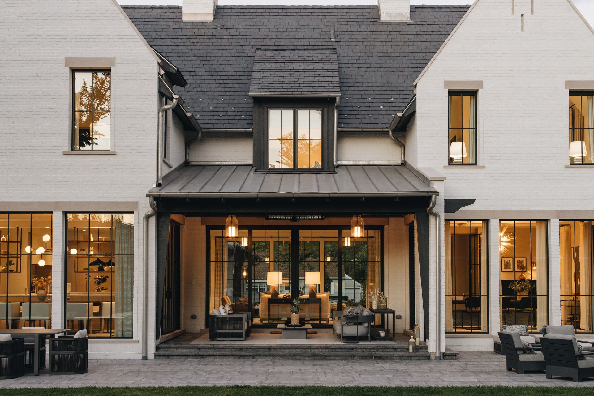 Front view of a modern gray house with a covered porch and warm-lit windows at dusk