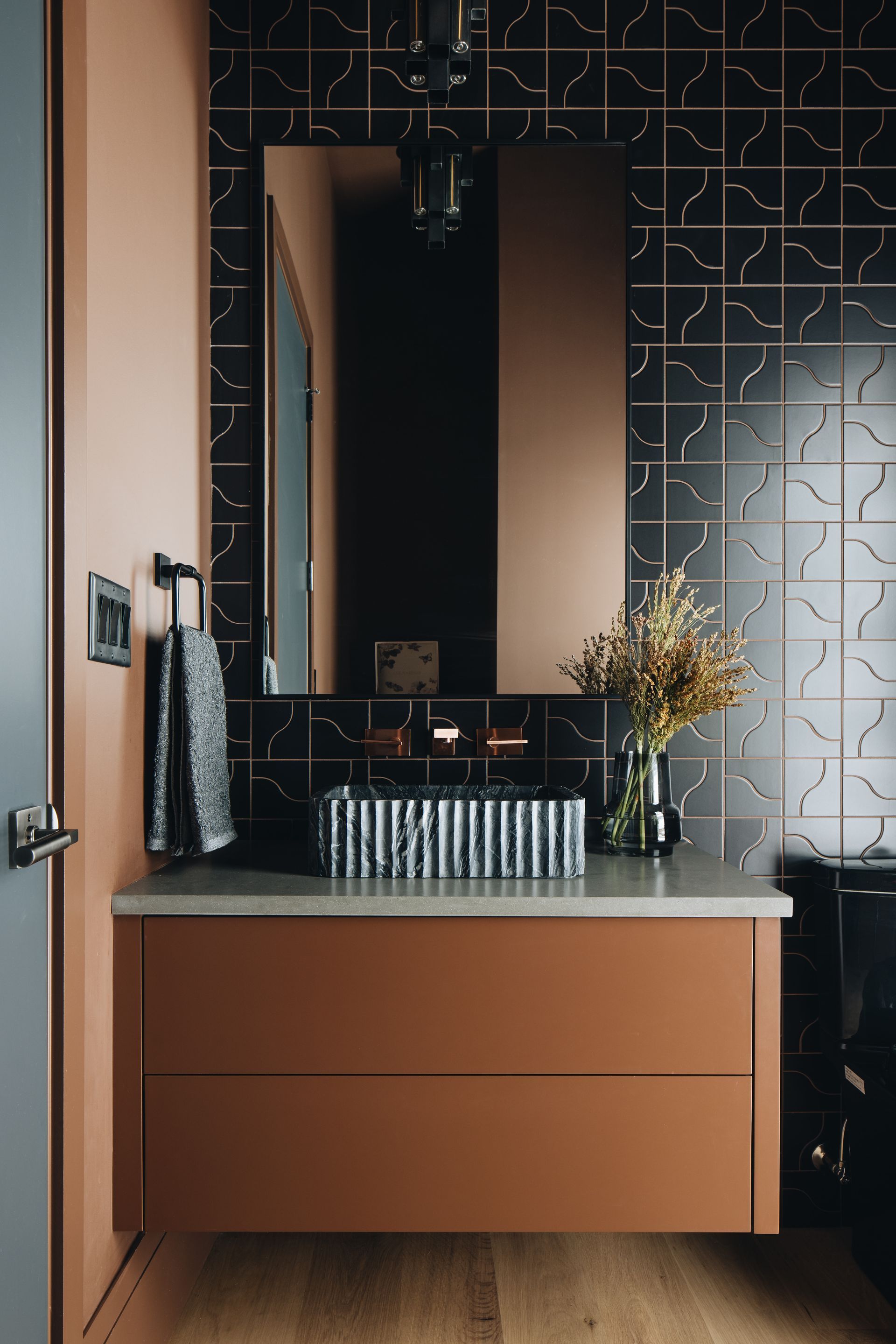 Modern bathroom vanity with copper cabinet, mirror, black tiled wall, and sink accessories