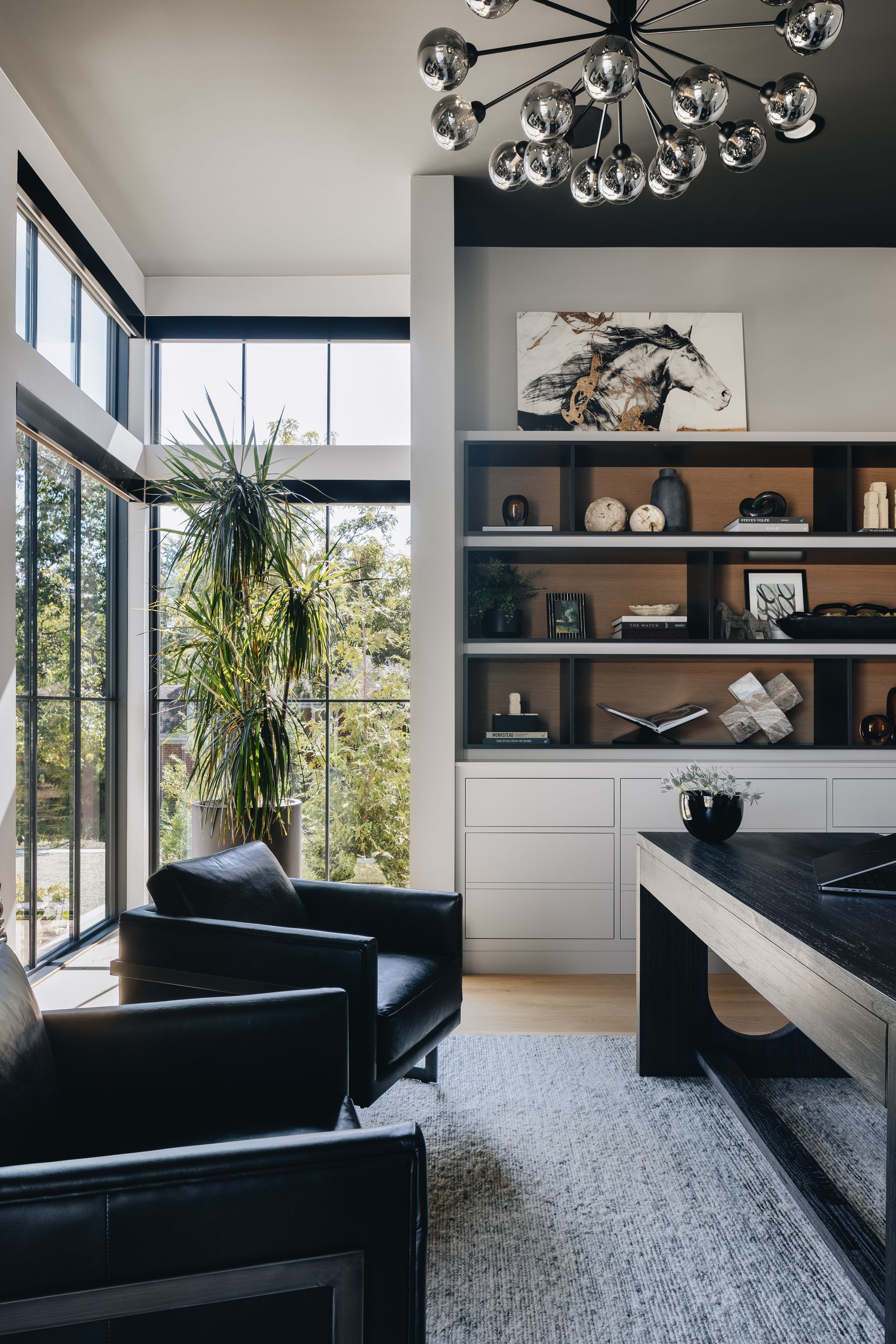 Modern living room with black chairs, built-in shelves, large windows, and a decorative chandelier