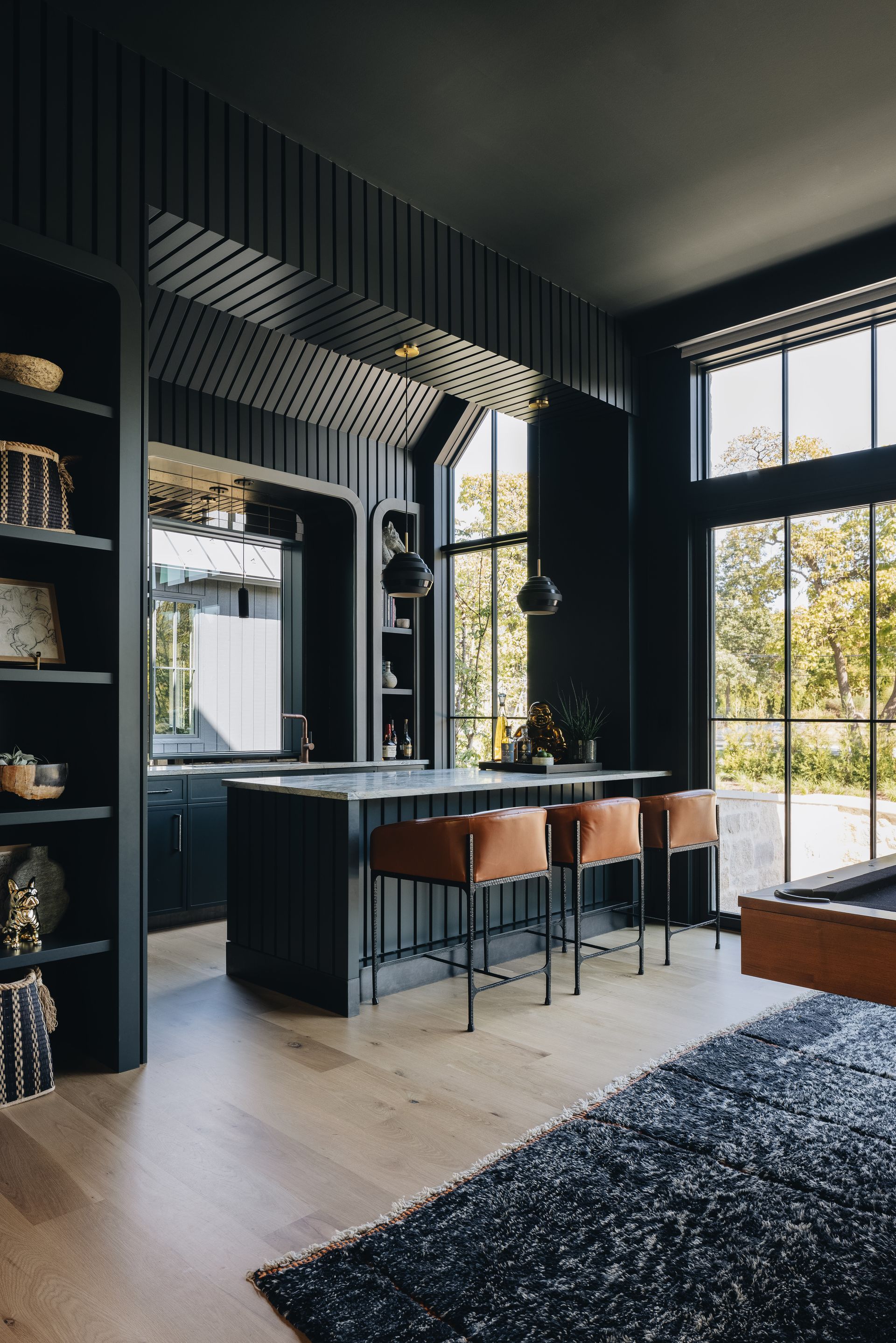 Modern kitchen with dark cabinetry, island seating, and large windows overlooking trees