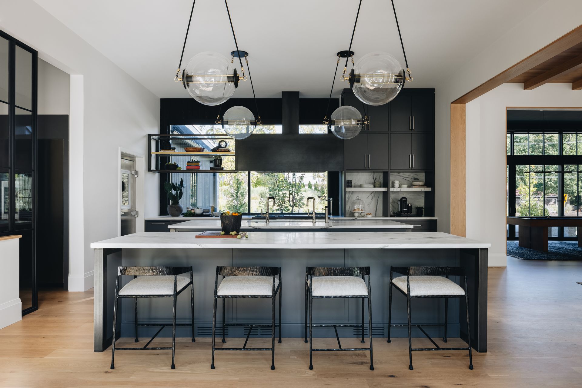 Modern kitchen with a large island, black cabinetry, pendant lights, and four stools
